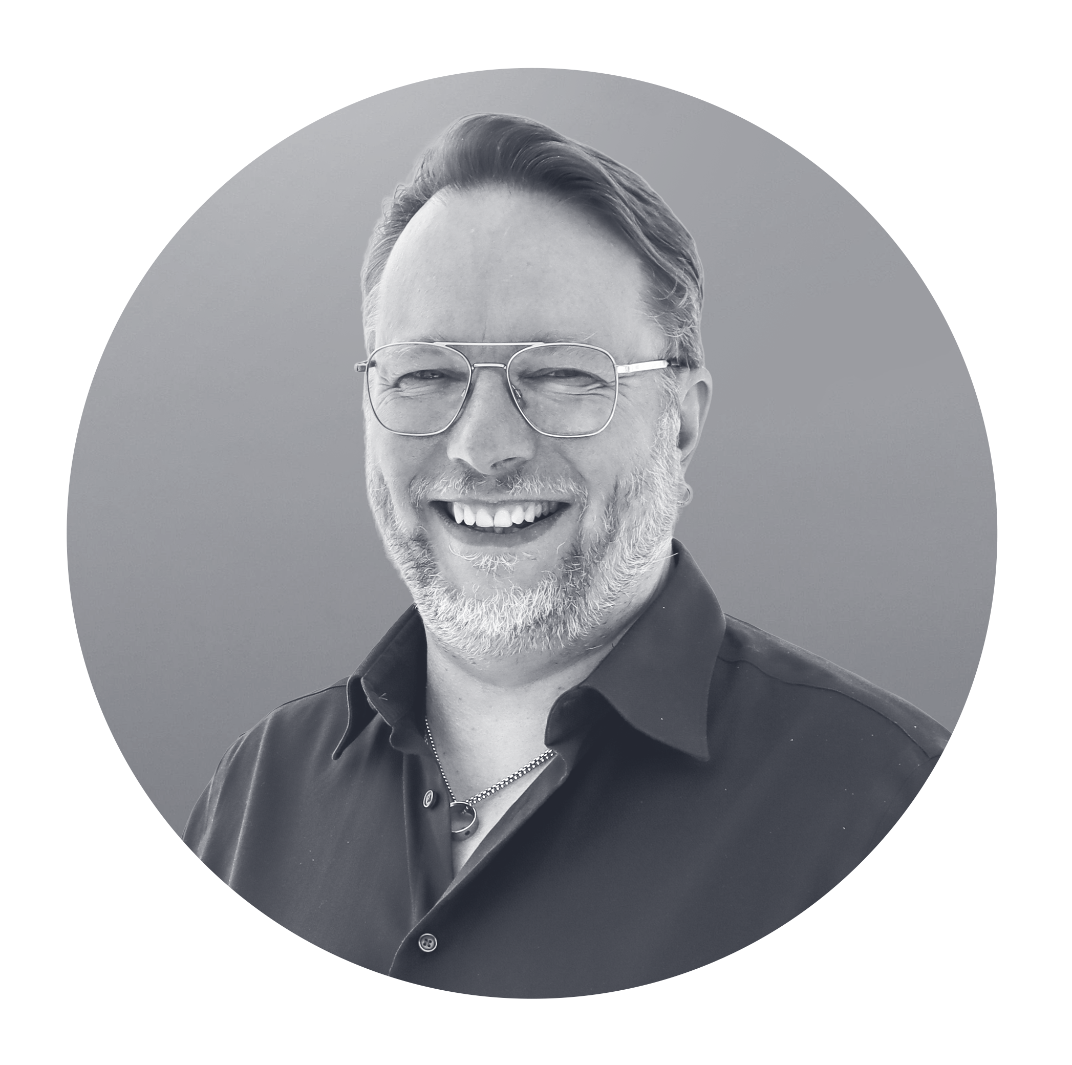 Black and white portrait of a smiling man with glasses, a beard, and short hair, wearing a dark collared shirt, against a gray background.