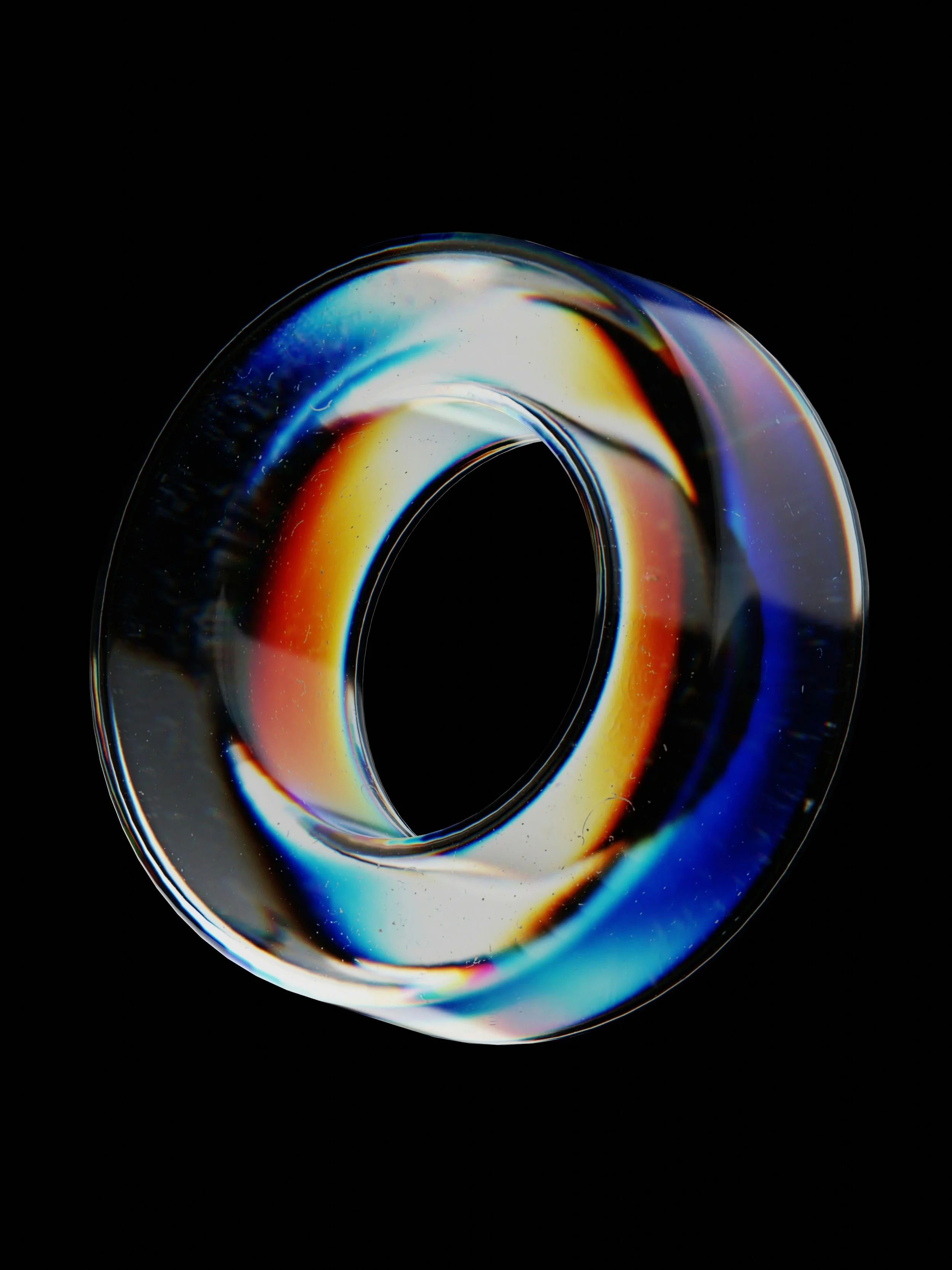 Close-up of a glass ring with a rainbow-like reflection against a black background.