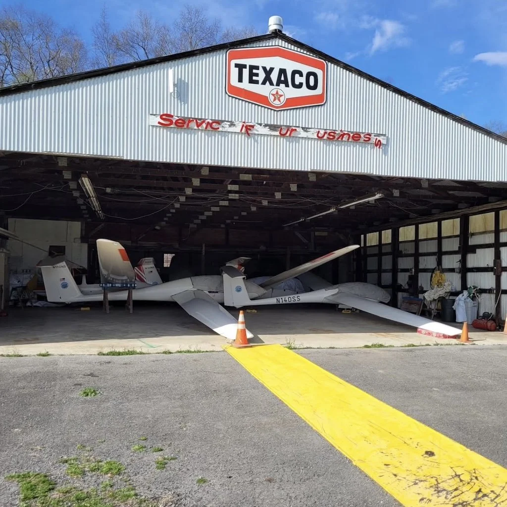 Gliders stored inside a Texaco aircraft hangar, with a yellow ramp leading inside.
