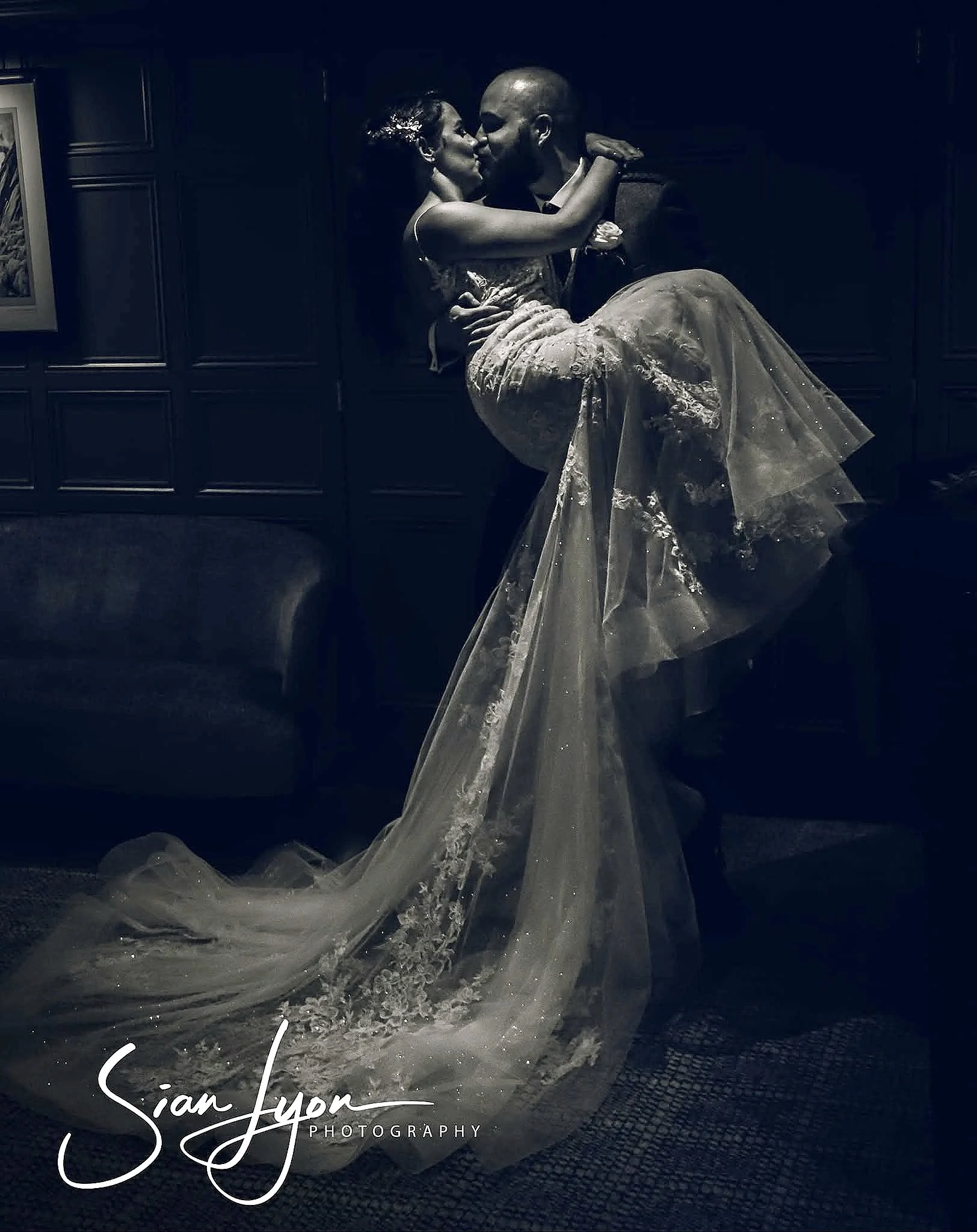 A couple dancing or sharing a kiss indoors, with the woman in a wedding dress and the man in a suit, capturing a romantic moment.