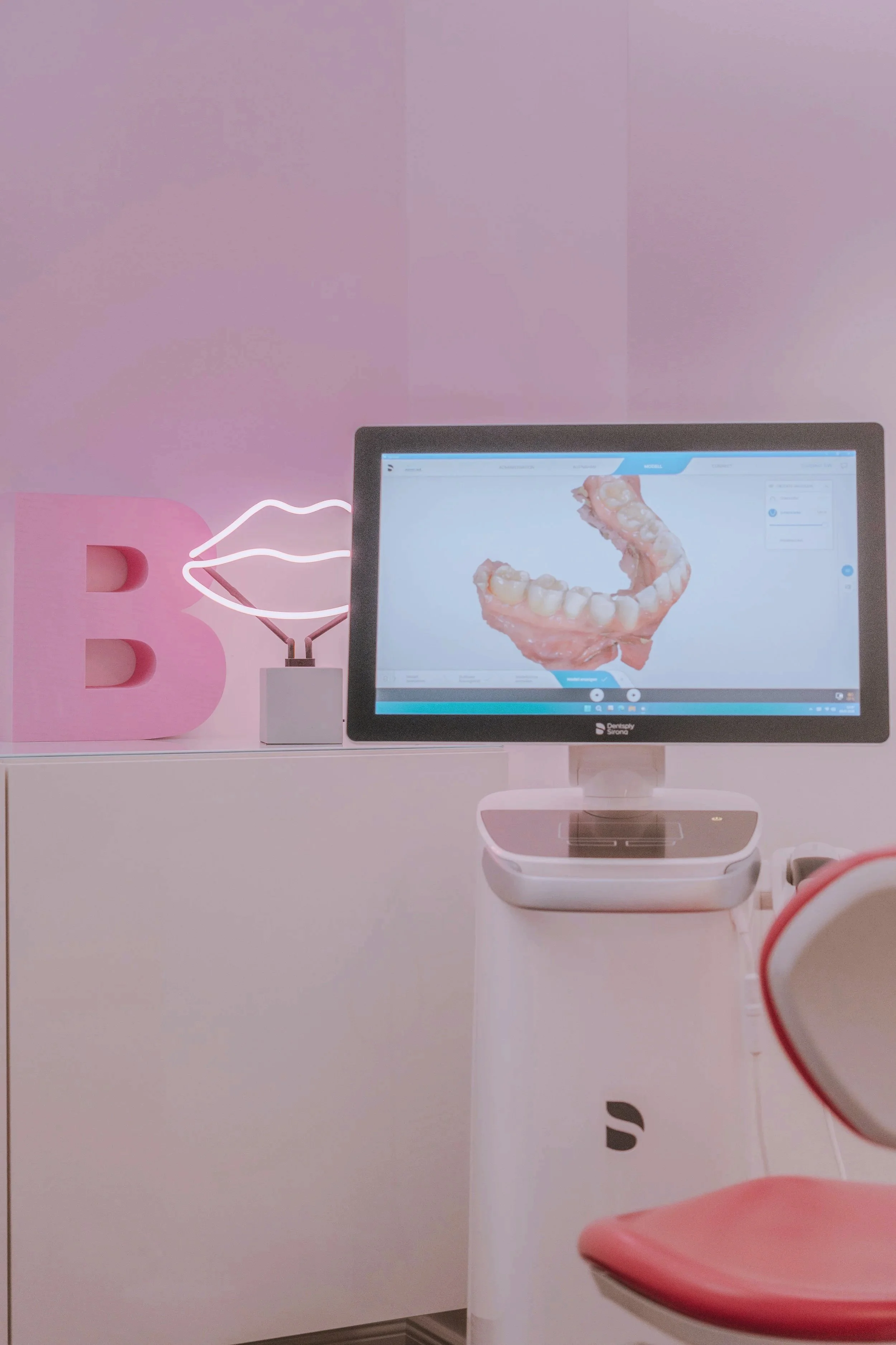 Ein Dentalgerät zeigt ein 3D-Modell eines menschlichen Ober- und Unterkiefer, wahrscheinlich für Zahnplanung oder Zahnsanierung. Davor steht ein leere Stuhl, der die freie Stelle signalisieren soll.