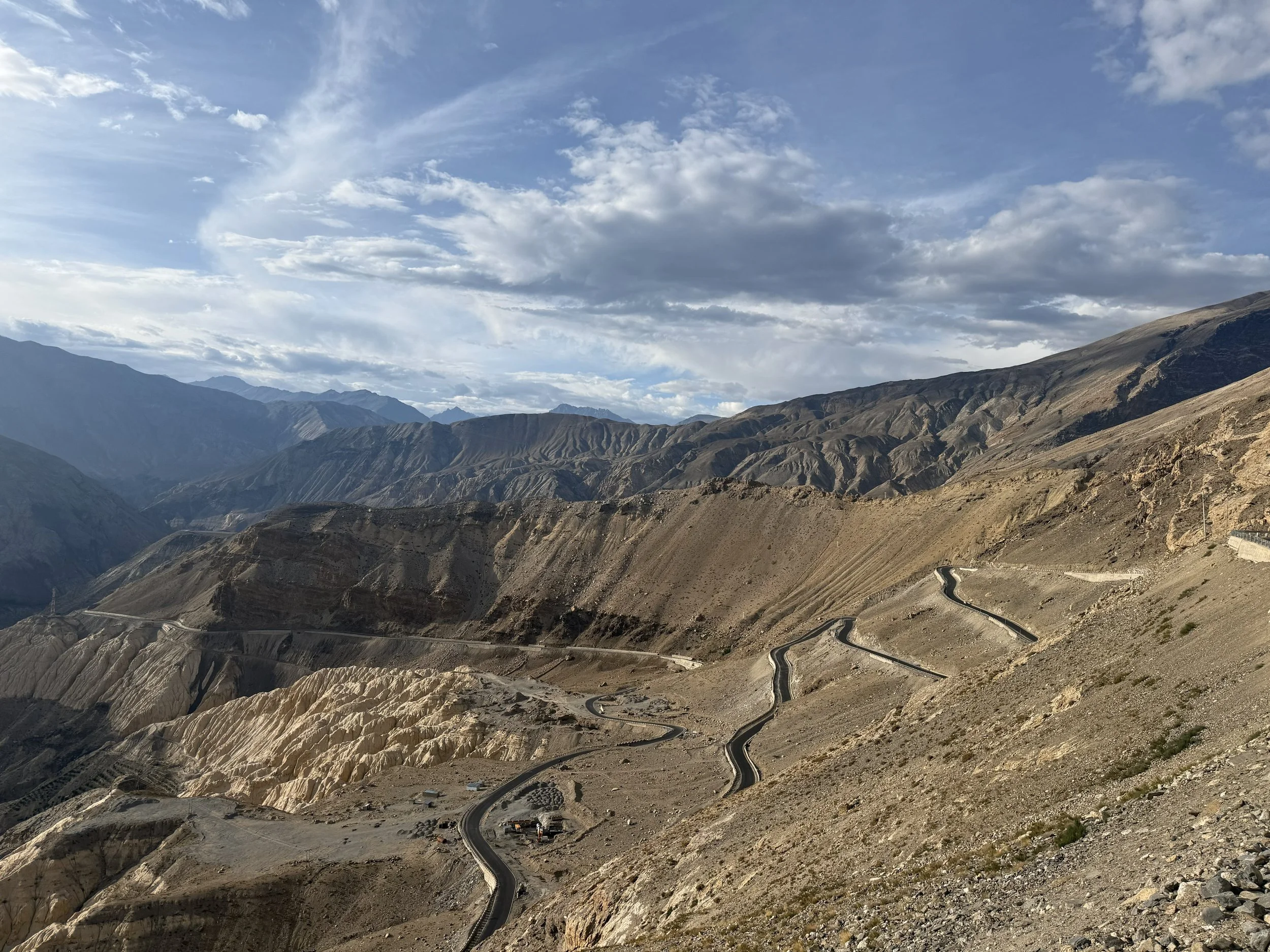 A winding mountain road cutting through Spiti’s stark, high-altitude landscape, with layered rocky mountains and wide open skies.
