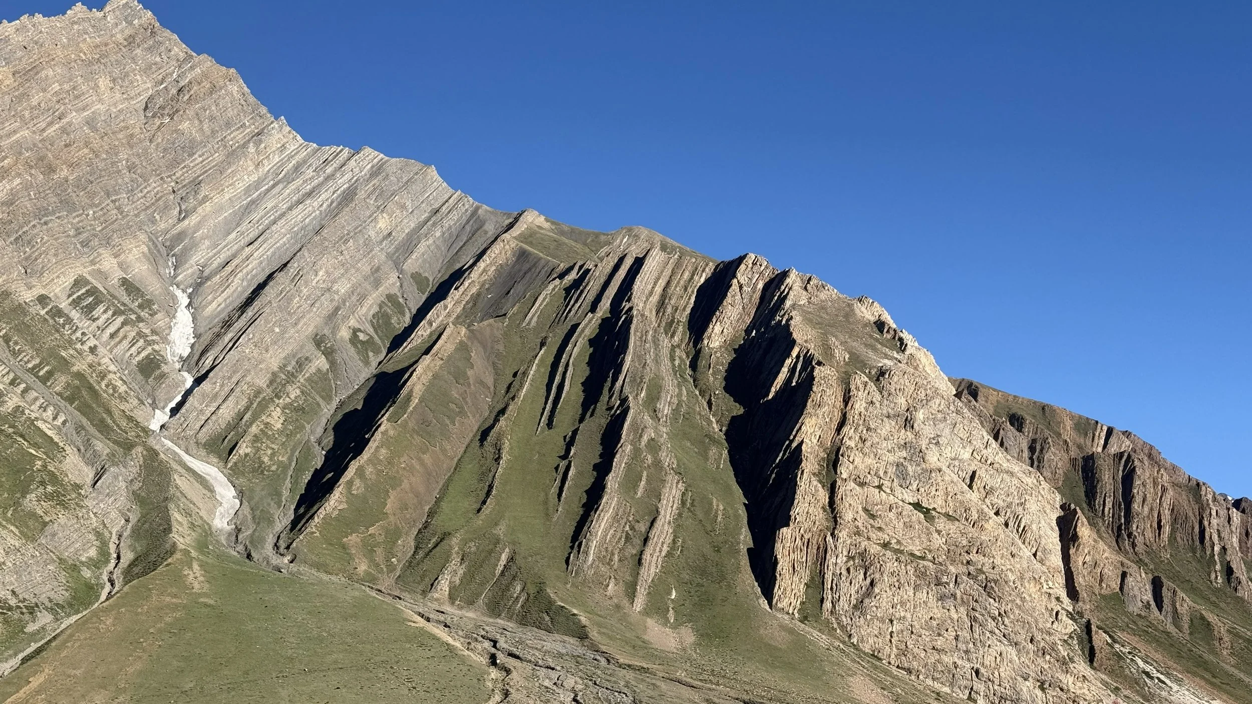 Spectacular view of rugged mountains with steep slopes and layered rock formations under a clear blue sky in Pin Valley