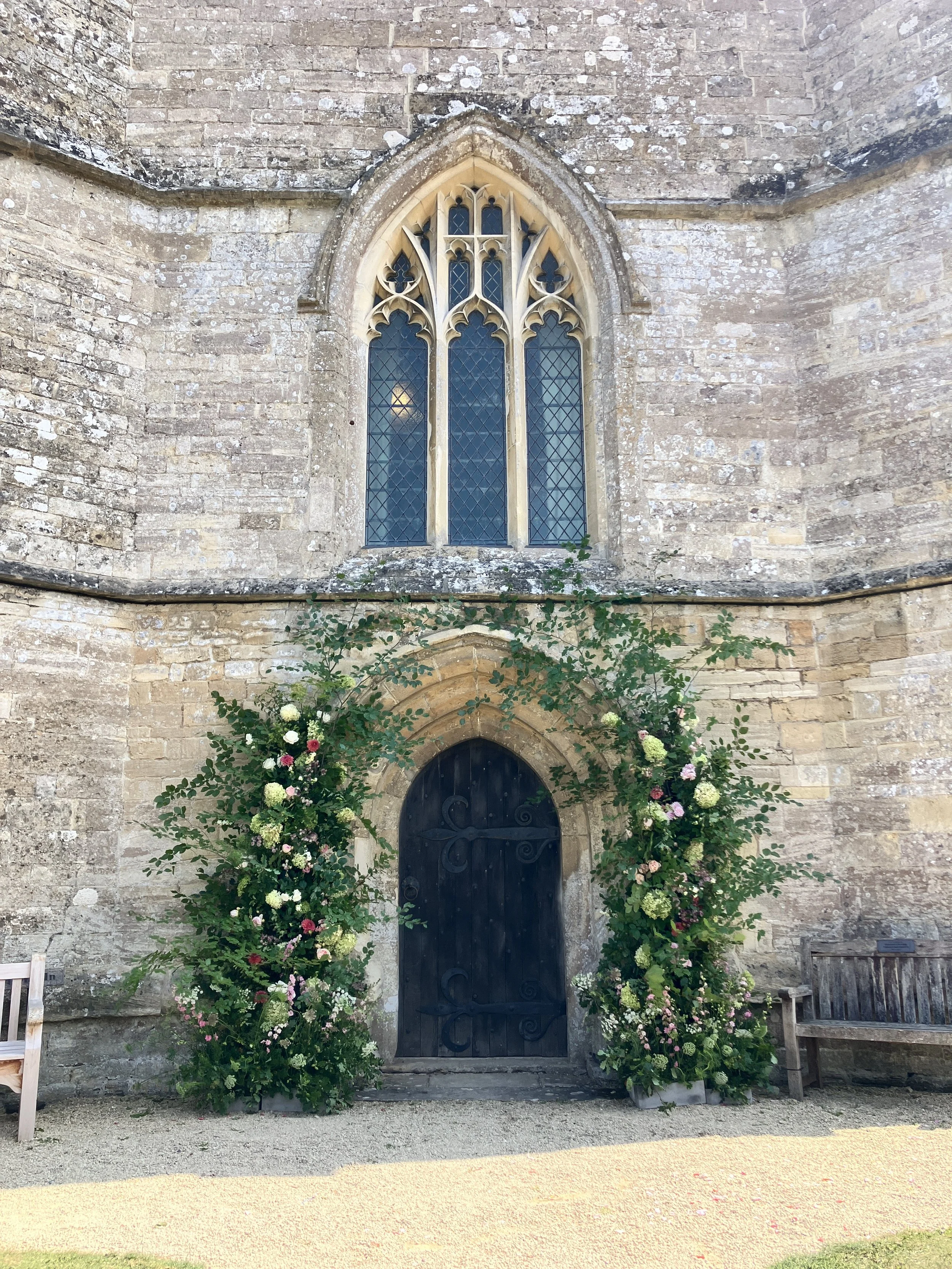 Outside the church with lovely floral display at St Mary the Virgin Church in Hawkesbury Upton, Gloucestershire before the wedding ceremony with organist Ben Humphries
