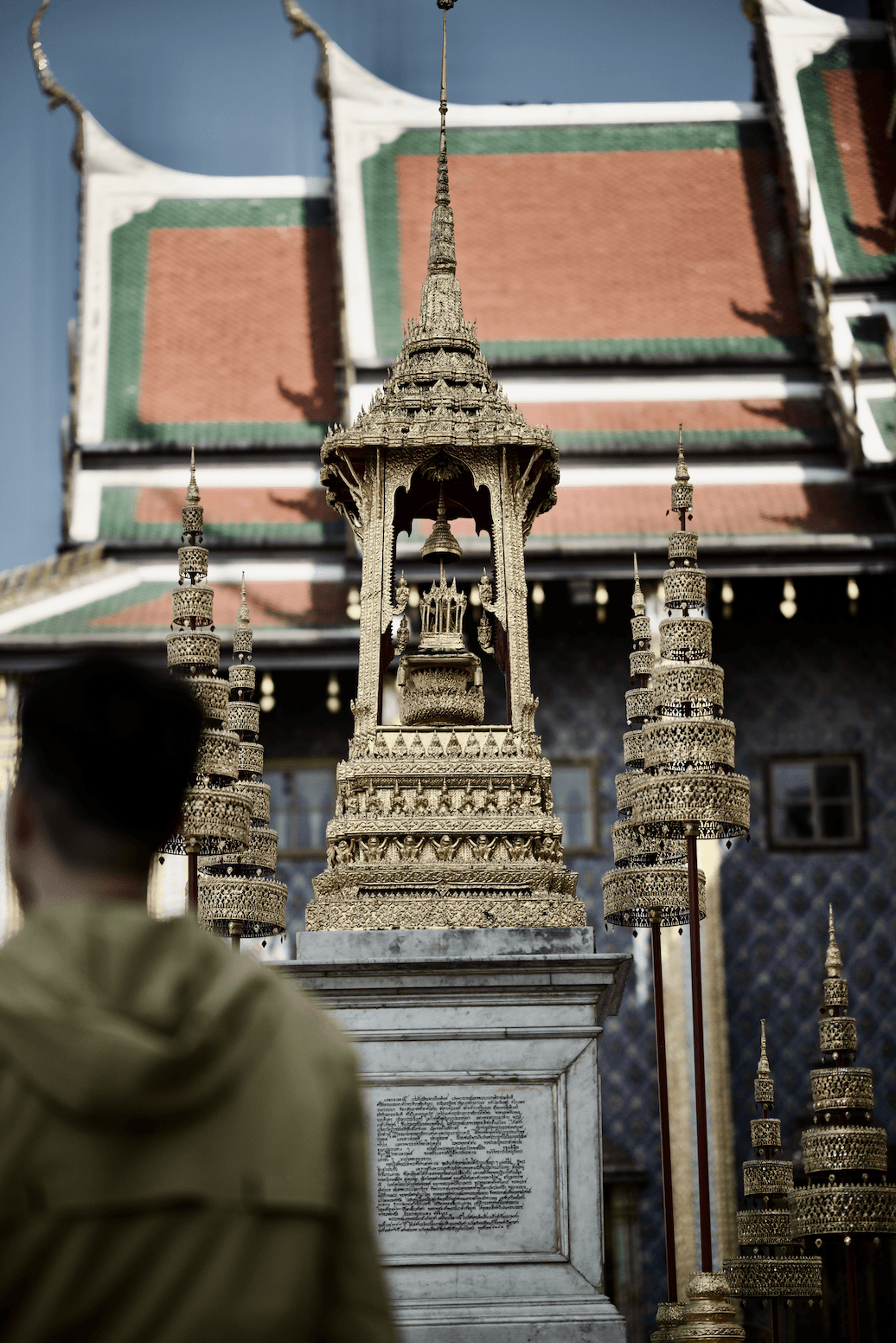 A small monument with multiple tiers, in front of a traditional Thai-style building in Royal Grand Palace in Bangkok.