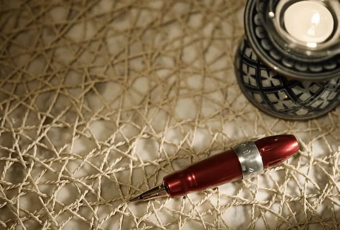 A tattoo machine with needle cartridge on texture background and blue ceramic candle base