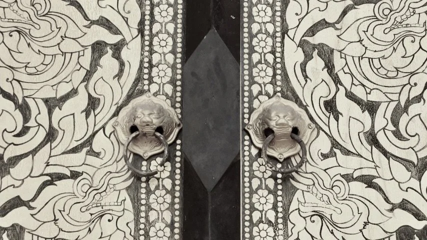 Close-up of ornate golden door handles shaped like lion heads , set against a decorative black and gold patterned door.