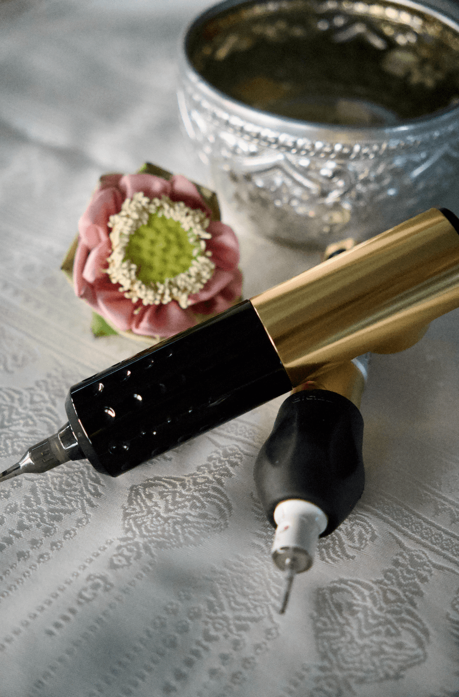 SMP tattoo machines next to the pink lotus with Thai silk cloth underneath - the sophisticated details of our SMP service.
