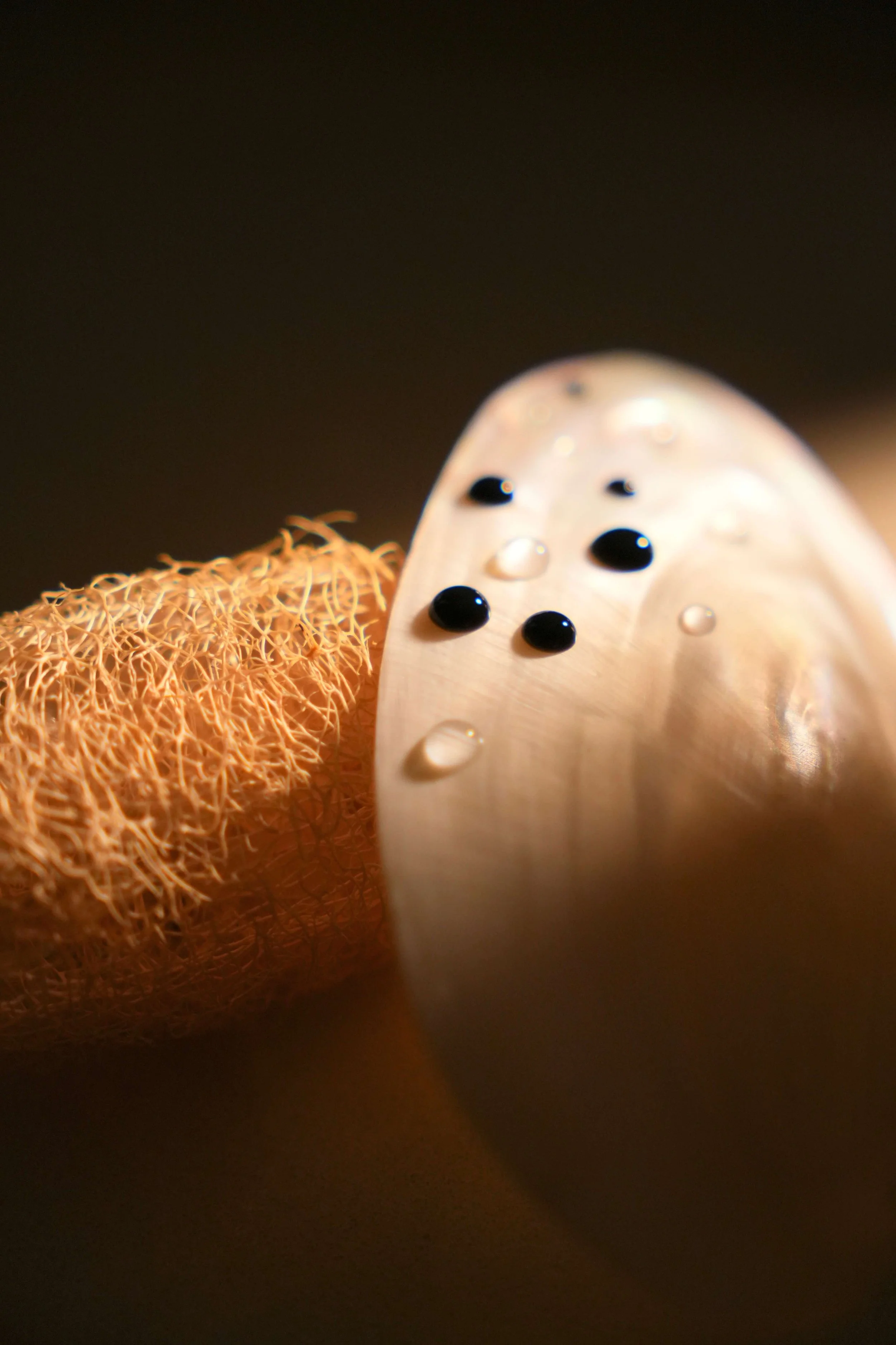 Close-up of a loofah sponge with water and tattoo pigment droplets on pearl shell.