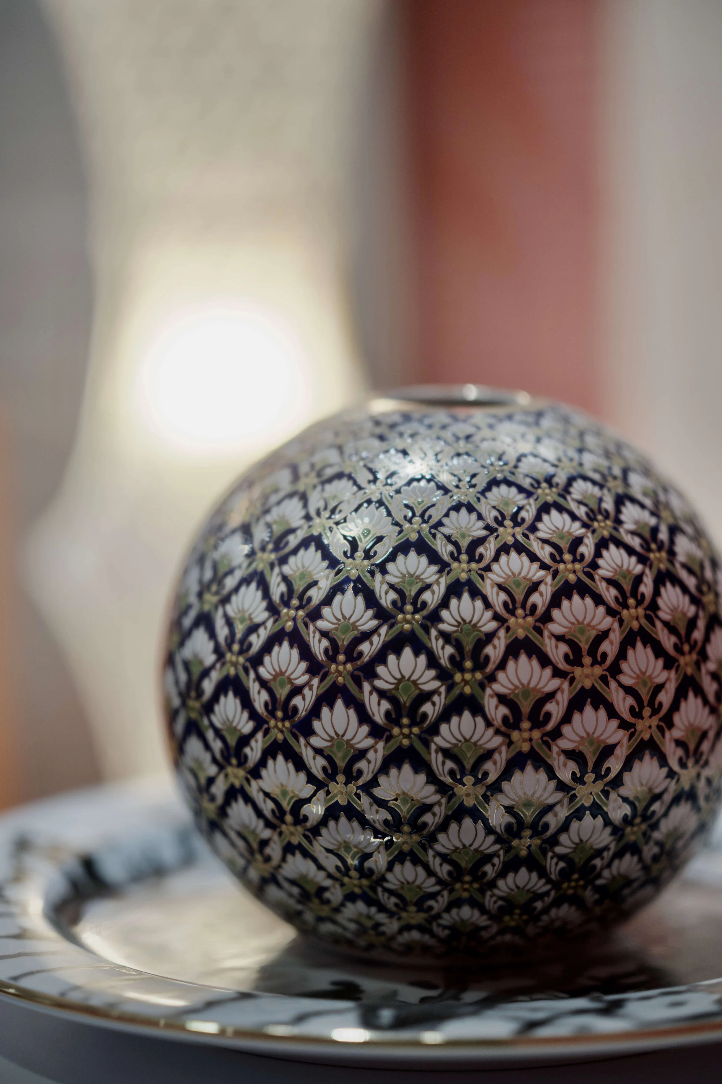 Close-up of an Eastern decorative round vase with intricate floral patterns in black, white, and gold on a reflective tray.