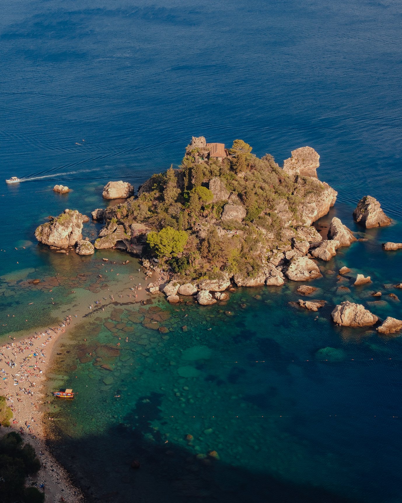 Aerial view of Isola Bella in Taormina with turquoise water and sandbar, capturing a cinematic Italian summer mood.