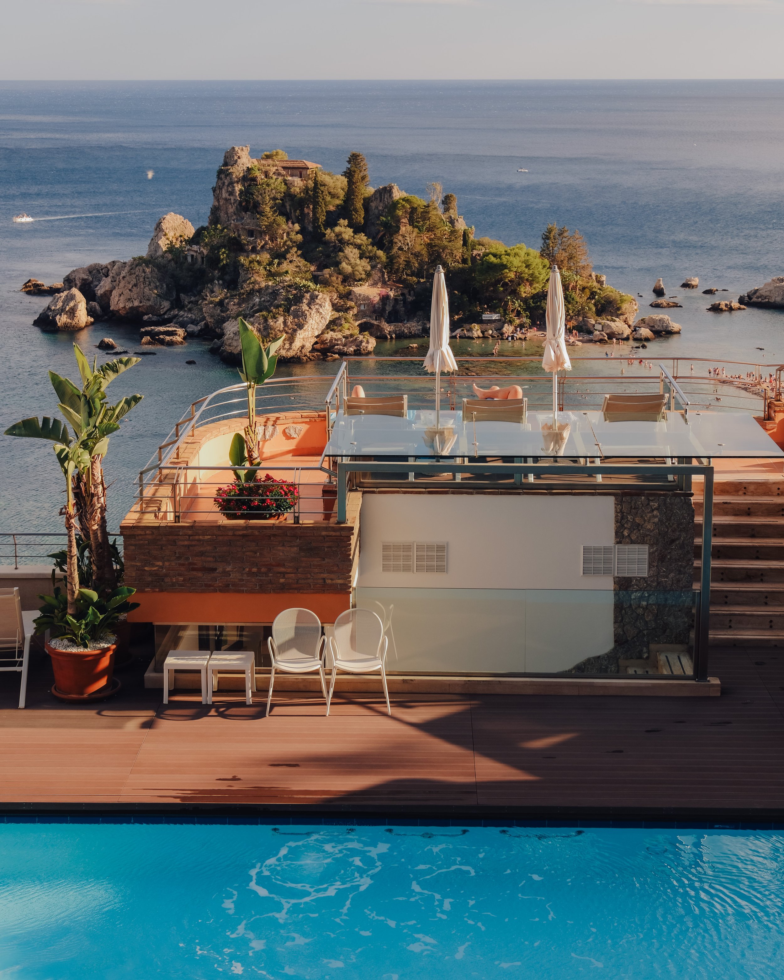 A modern rooftop terrace with glass railings offering a stunning view of Isola Bella below.