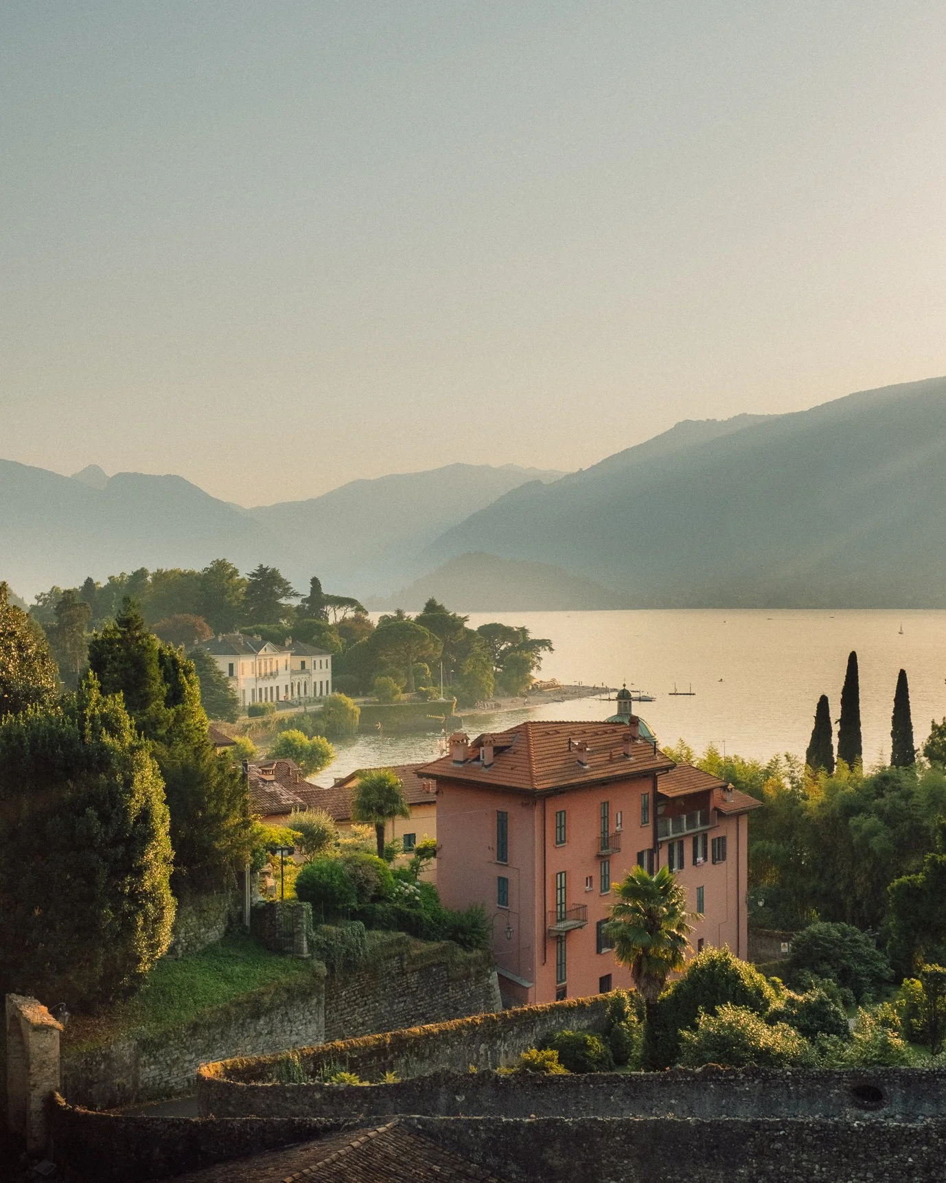 A romantic, hazy view of a peach-colored Italian villa nestled on a hillside during golden hour.