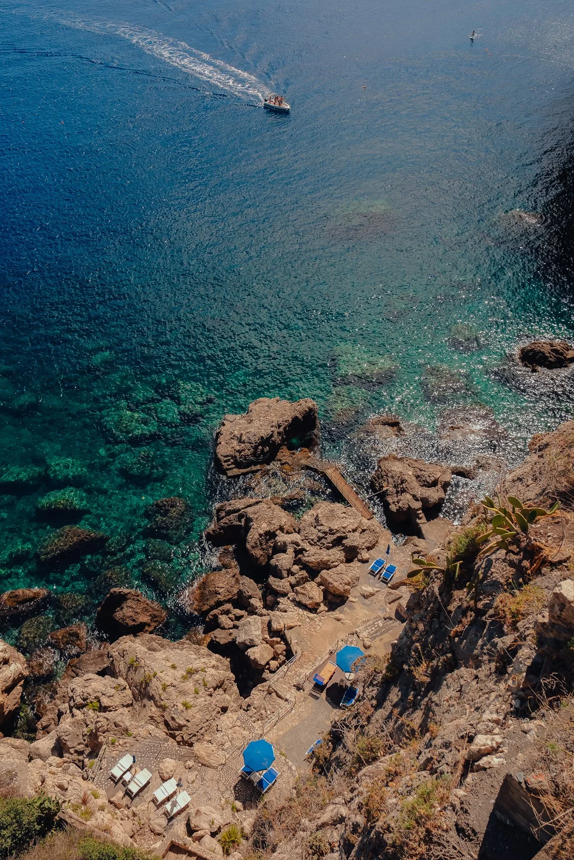 High-contrast aerial texture of deep blue sea water crashing against jagged coastal rocks.