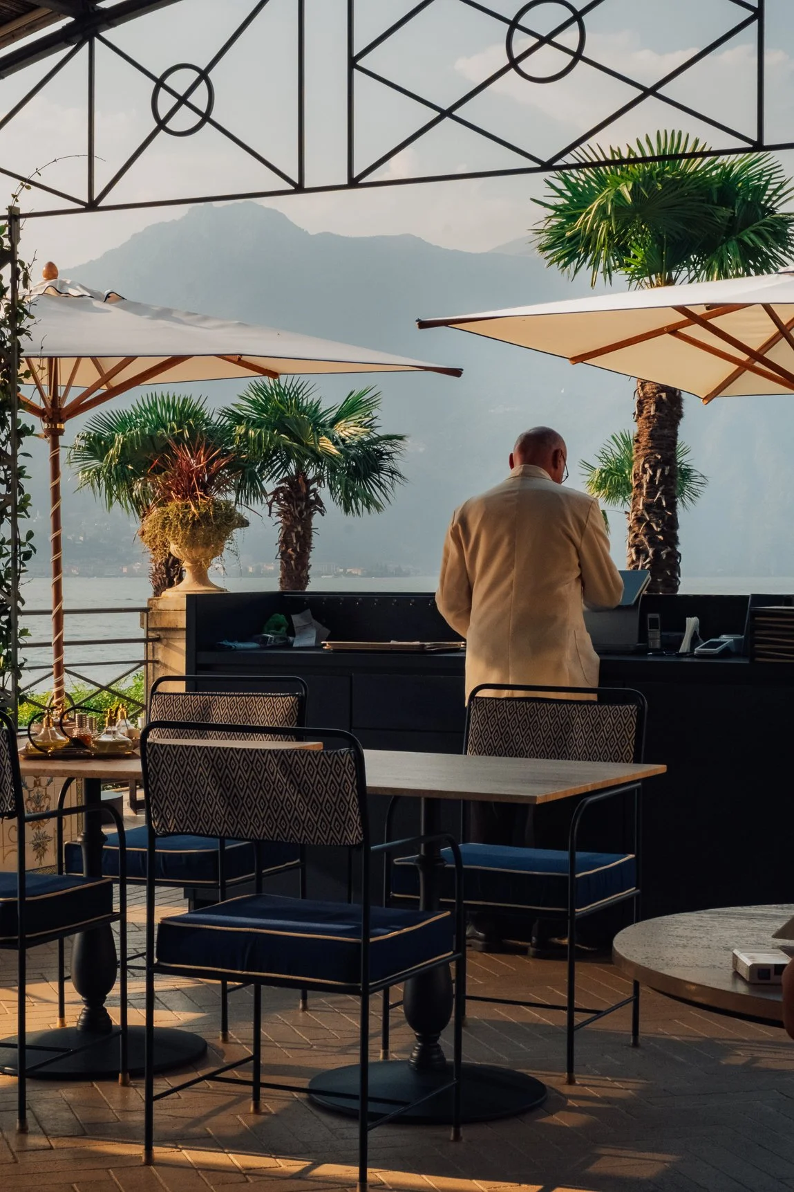 A cinematic shot of a man in a beige suit overlooking Lake Como from a grand hotel terrace.