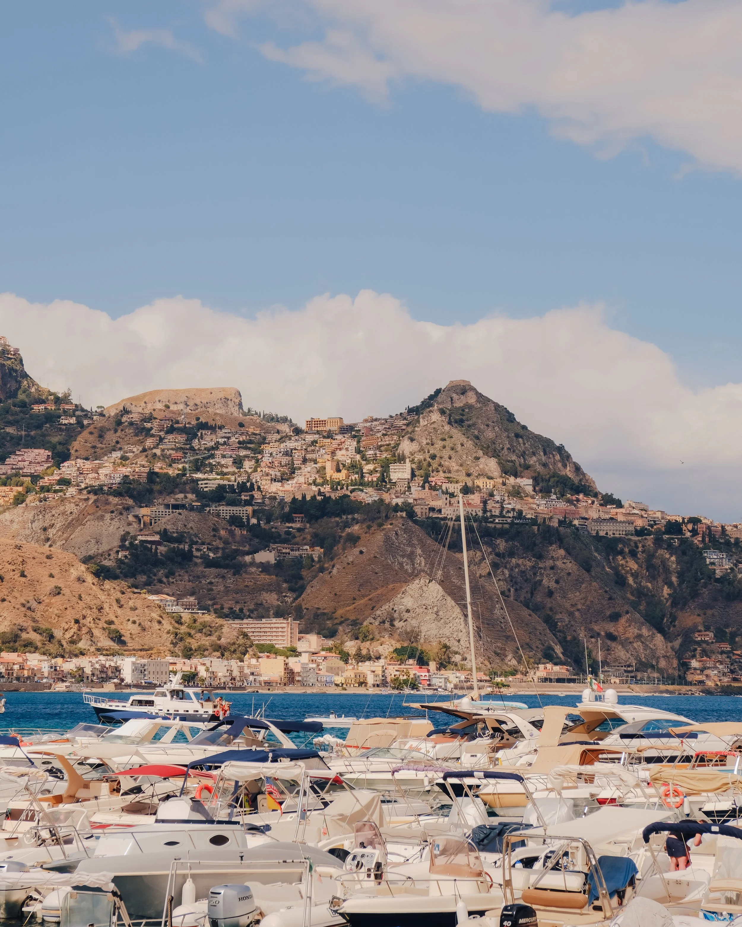White boats moored in a calm harbor with dramatic mountains rising in the background.