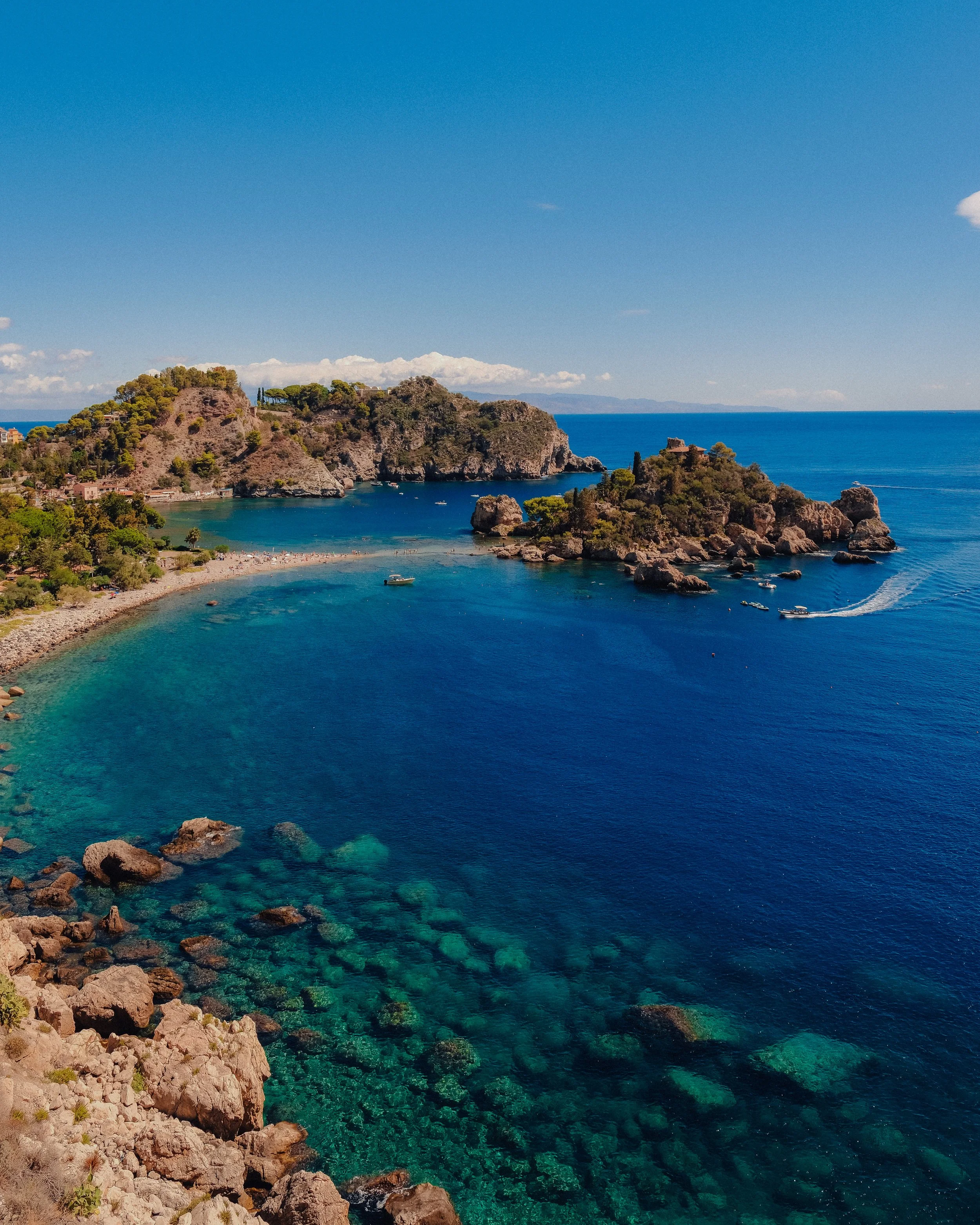 A wide landscape shot of Isola Bella and the coastline featuring deep blue ocean tones.