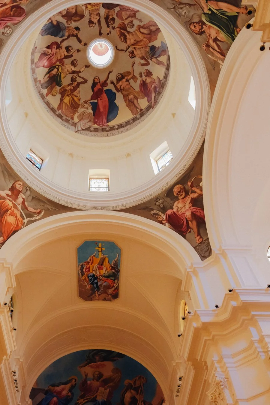 Interior view of a church ceiling with elaborate religious fresco paintings depicting biblical scenes and figures, including Jesus and saints.
