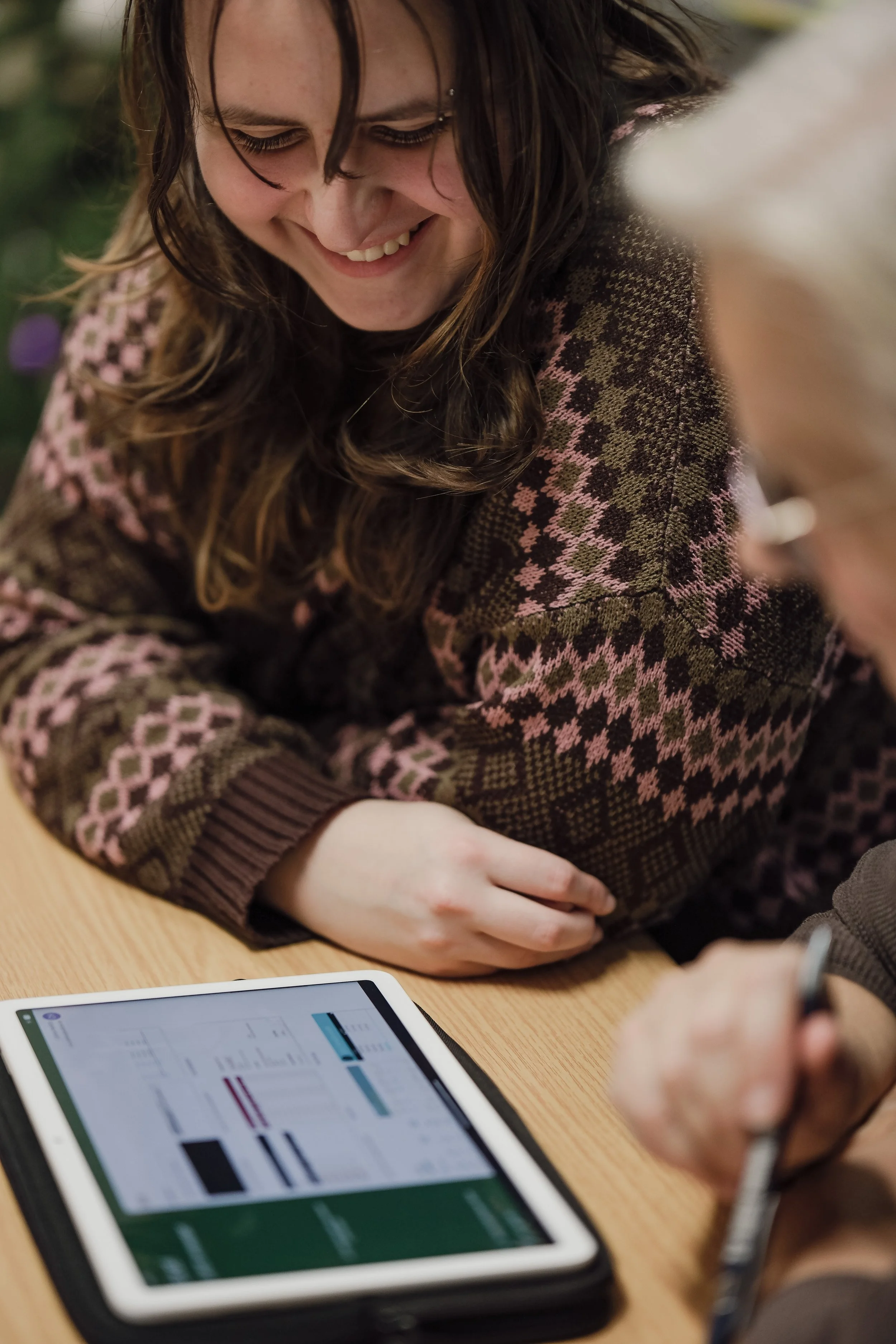 Zwei Menschen von Sonay soziales Leben e.V. im Projekt Teilhabe-Hilfe-Card Jugendliche und Senioren sitzen an einem Tisch, einer zeigt auf einen Tablet-Computer mit Diagrammen, die andere lächelt nearby.