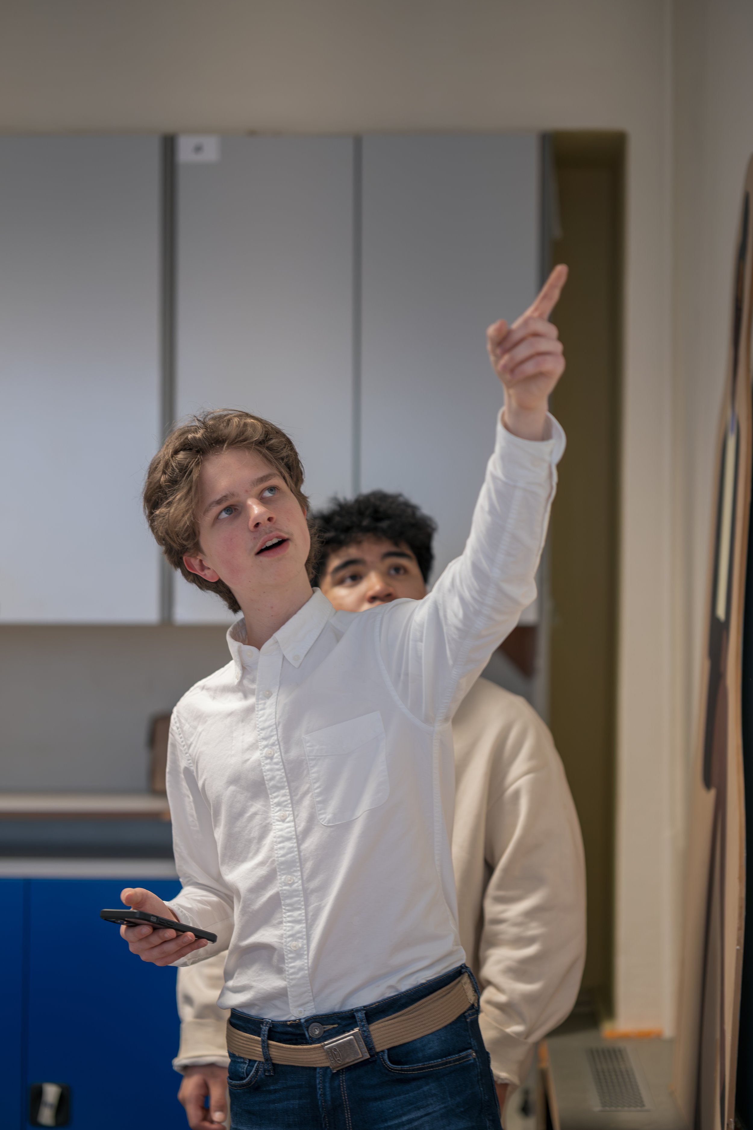 Ein junger Mann  Sonay soziales Leben e.V. im Projekt Teilhabe-Hilfe-Card Jugendliche und Seniorenin weißem Hemd zeigt auf eine Tafel, während ein anderer junger Mann im Hintergrund zuschaut.