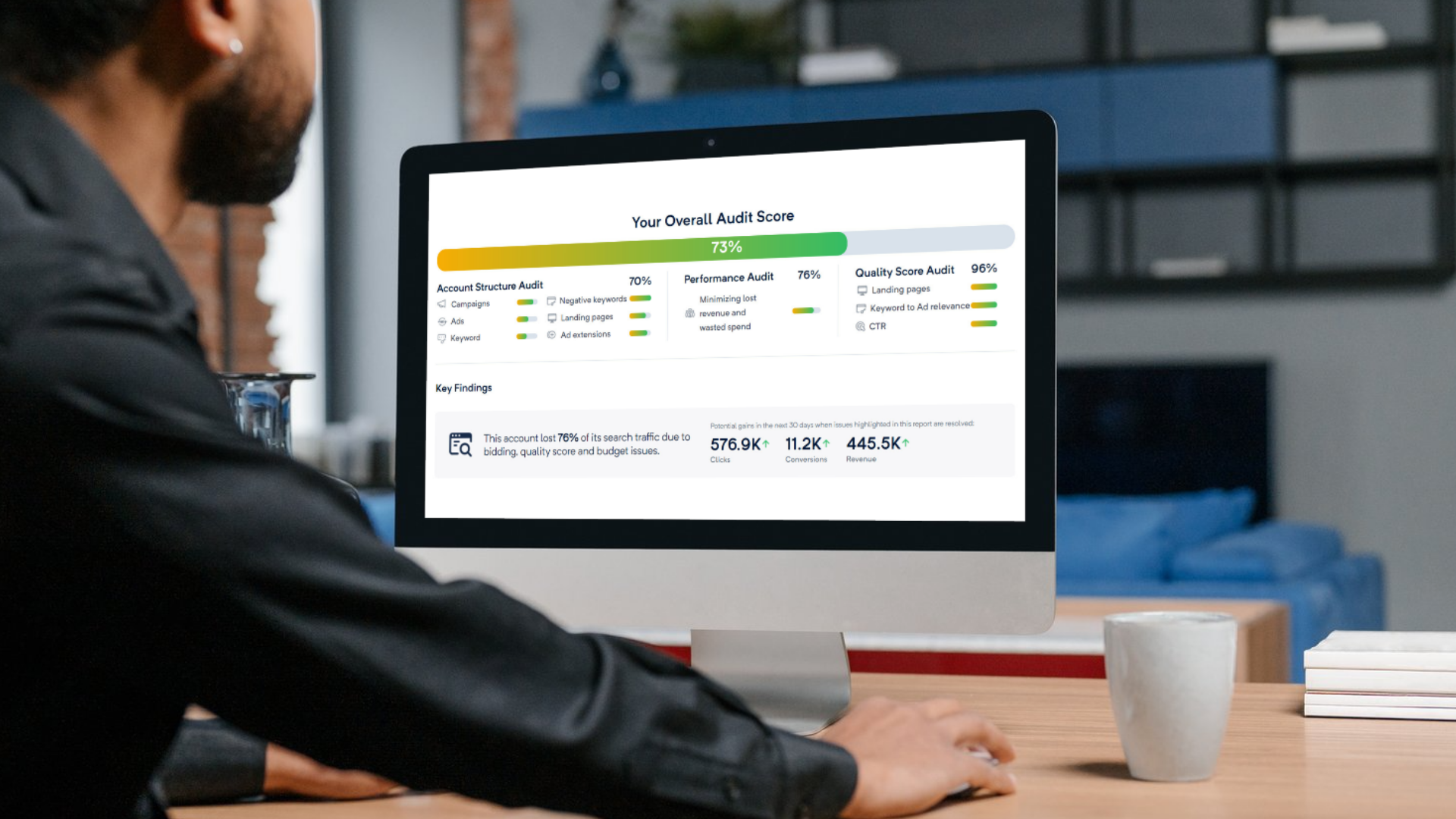 Person working at a desk viewing an audit score report on an Apple iMac computer, with a mug and some books on the desk.