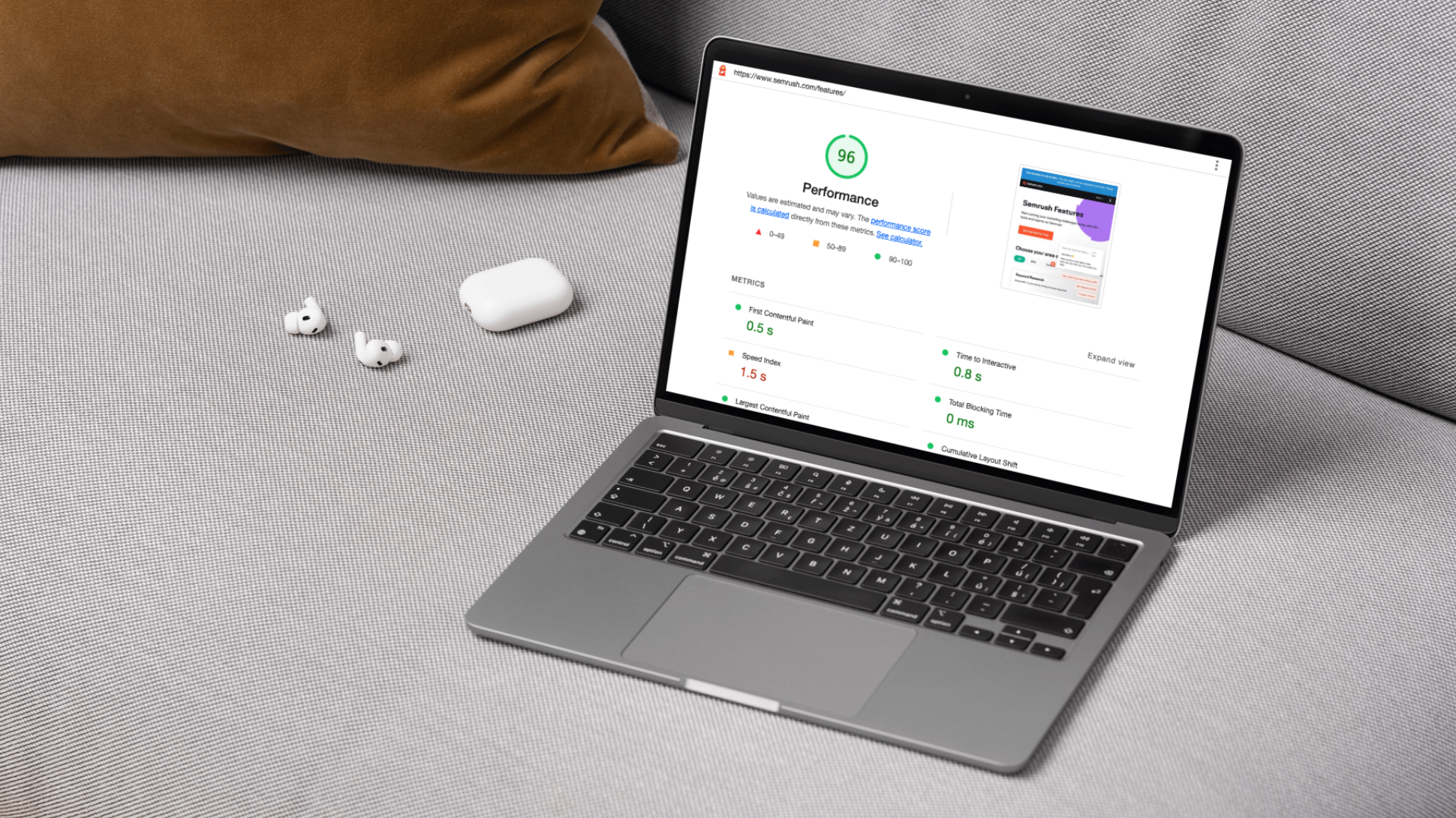 A gray laptop displaying a performance analysis webpage, placed on a gray textured surface next to a pair of white wireless earbuds and their charging case, with a brown pillow and a gray sofa in the background.