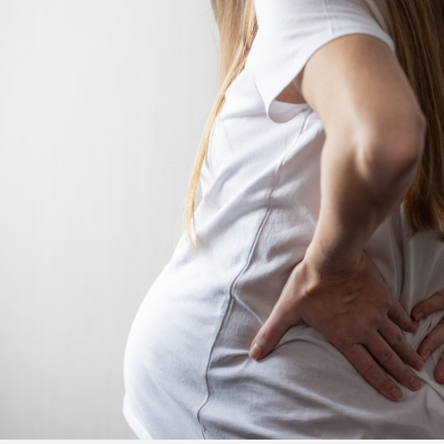Close-up of a woman holding her lower back in pain while wearing a white shirt.