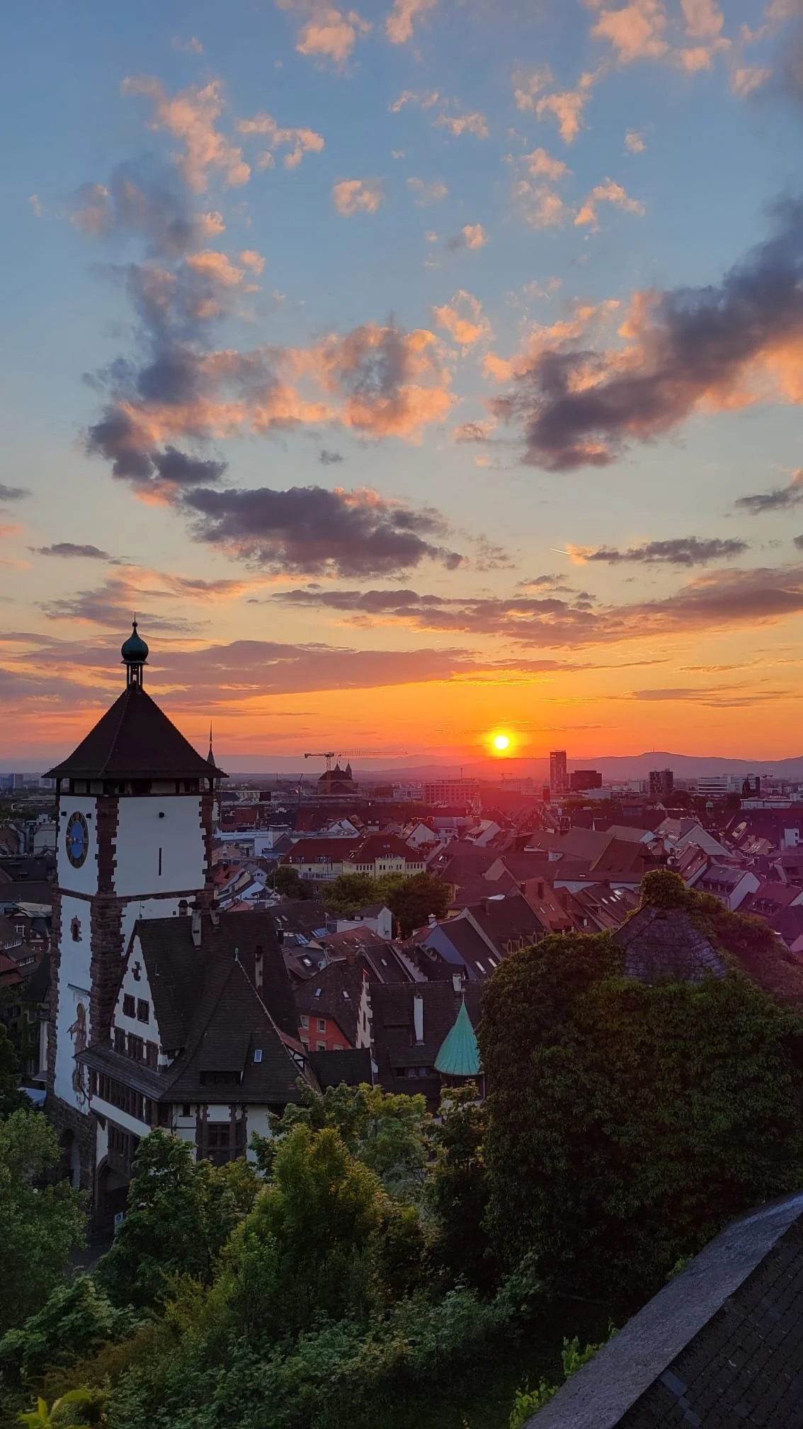 Sunset over Freiburg city with a prominent church tower and colorful sky with clouds.