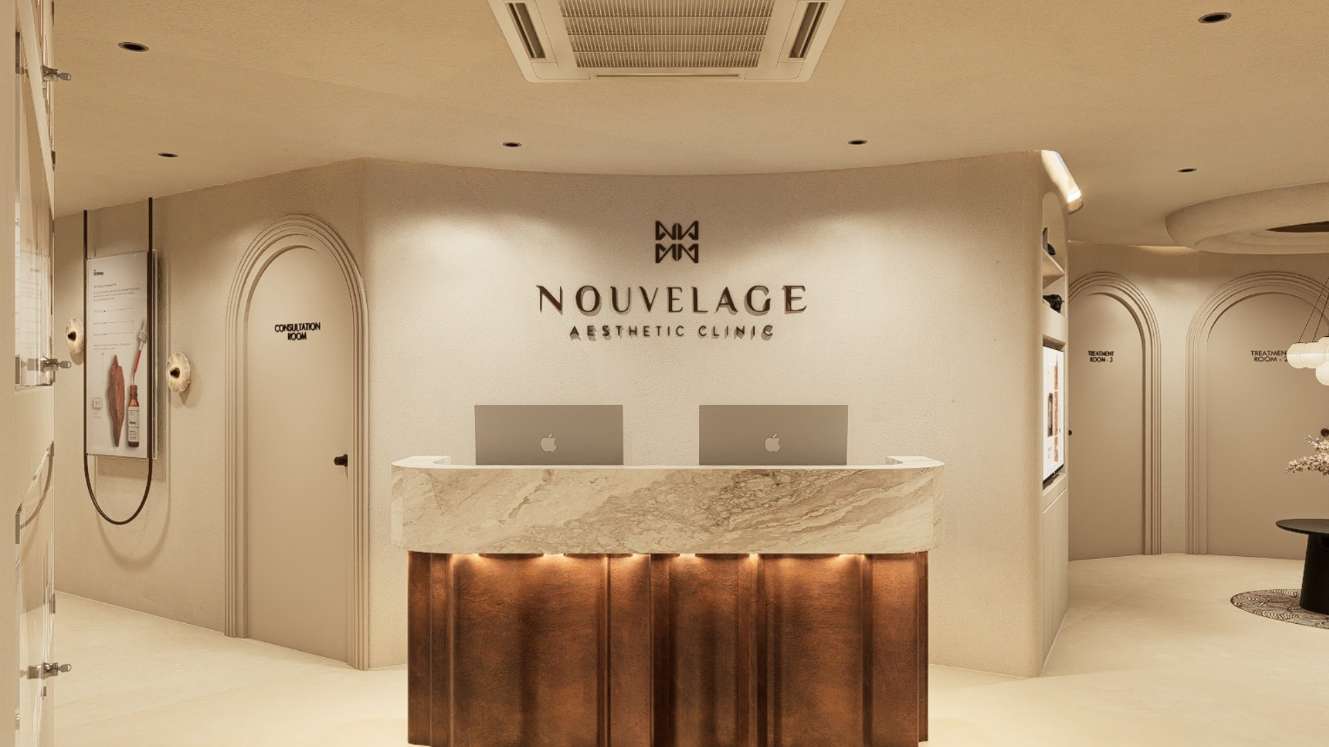 Reception area of Nouelage Aesthetic Clinic with a marble front desk, two Apple computers, and signs for consultation and treatment rooms.