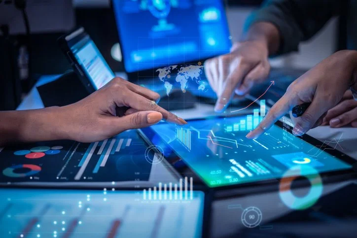 People using digital devices and touchscreen tablets displaying financial and data analytics graphs.