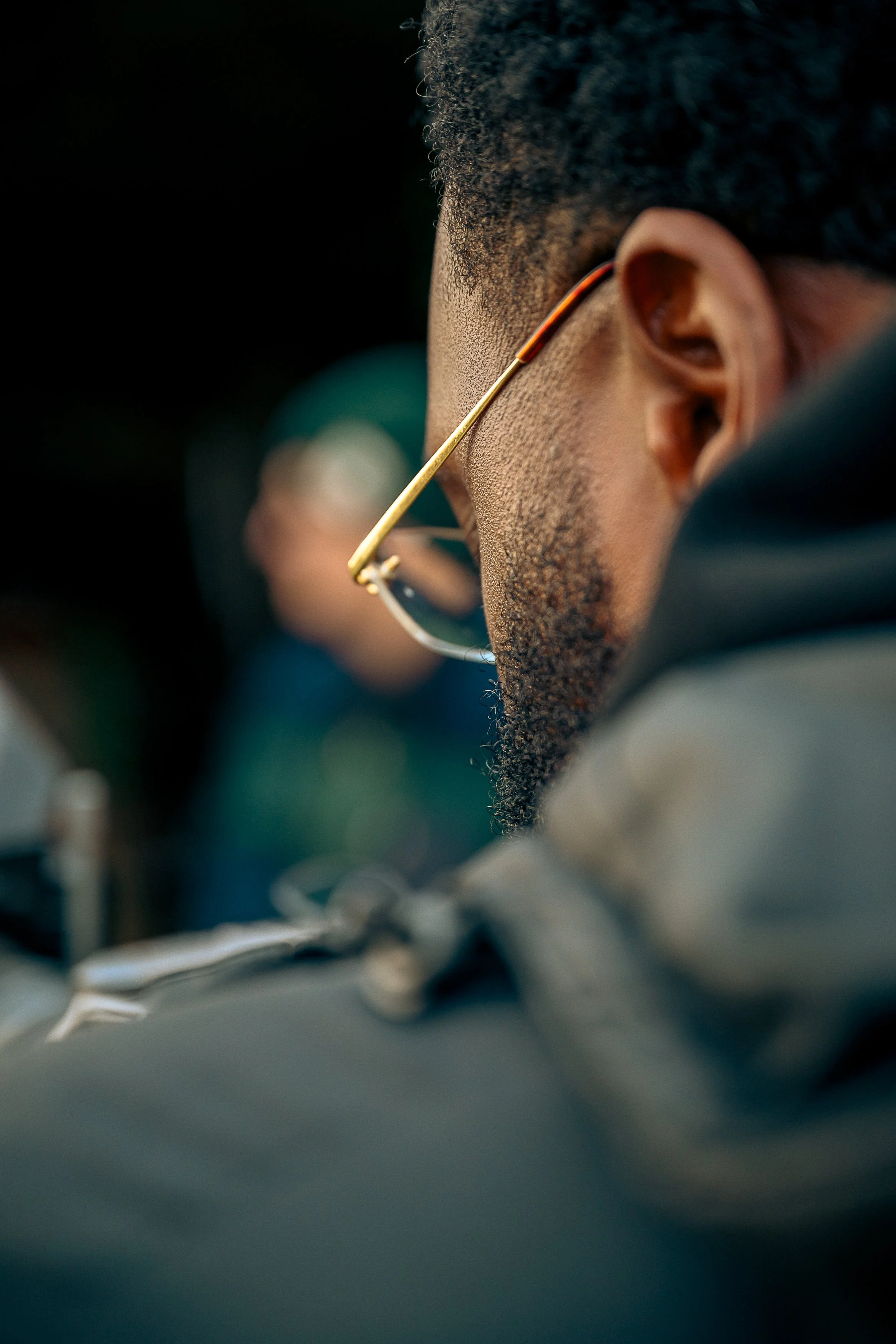 Close-up of a person's face wearing glasses, with short curly hair and a beard, looking downward.