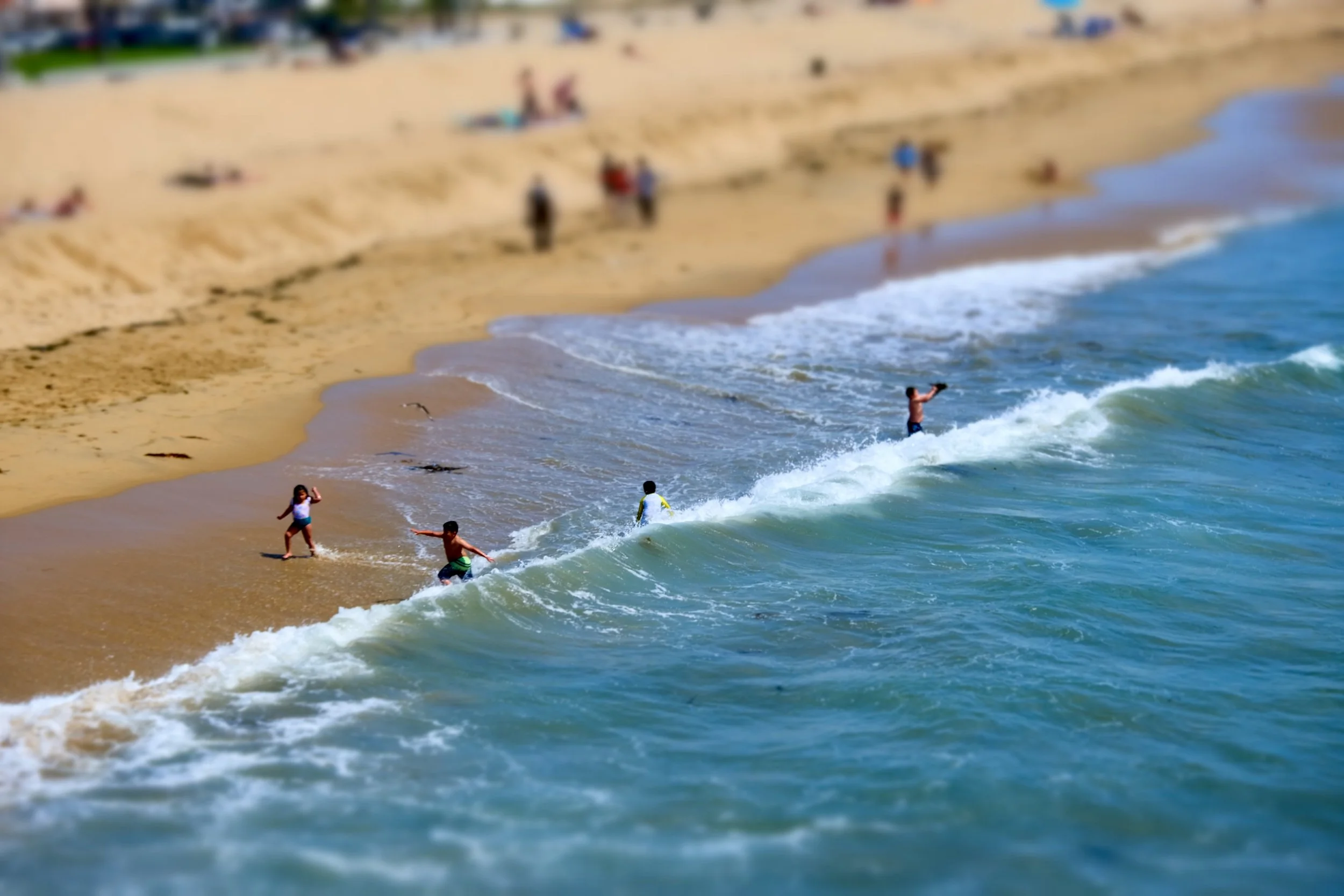 People enjoying a day at the beach, some swimming in the water and others walking along the sandy shoreline.