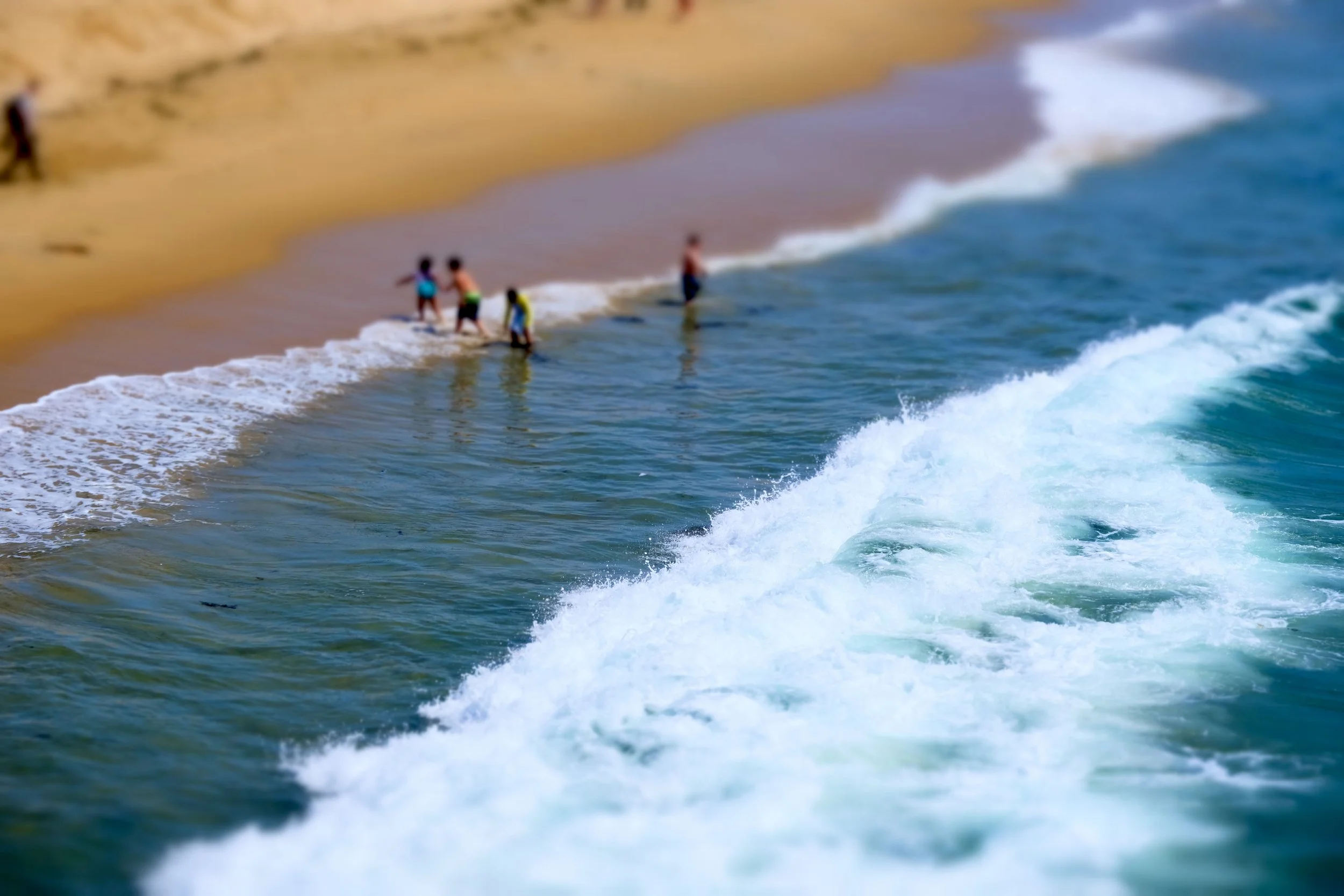 Children and an adult playing at the shoreline of a sandy beach with waves crashing in.