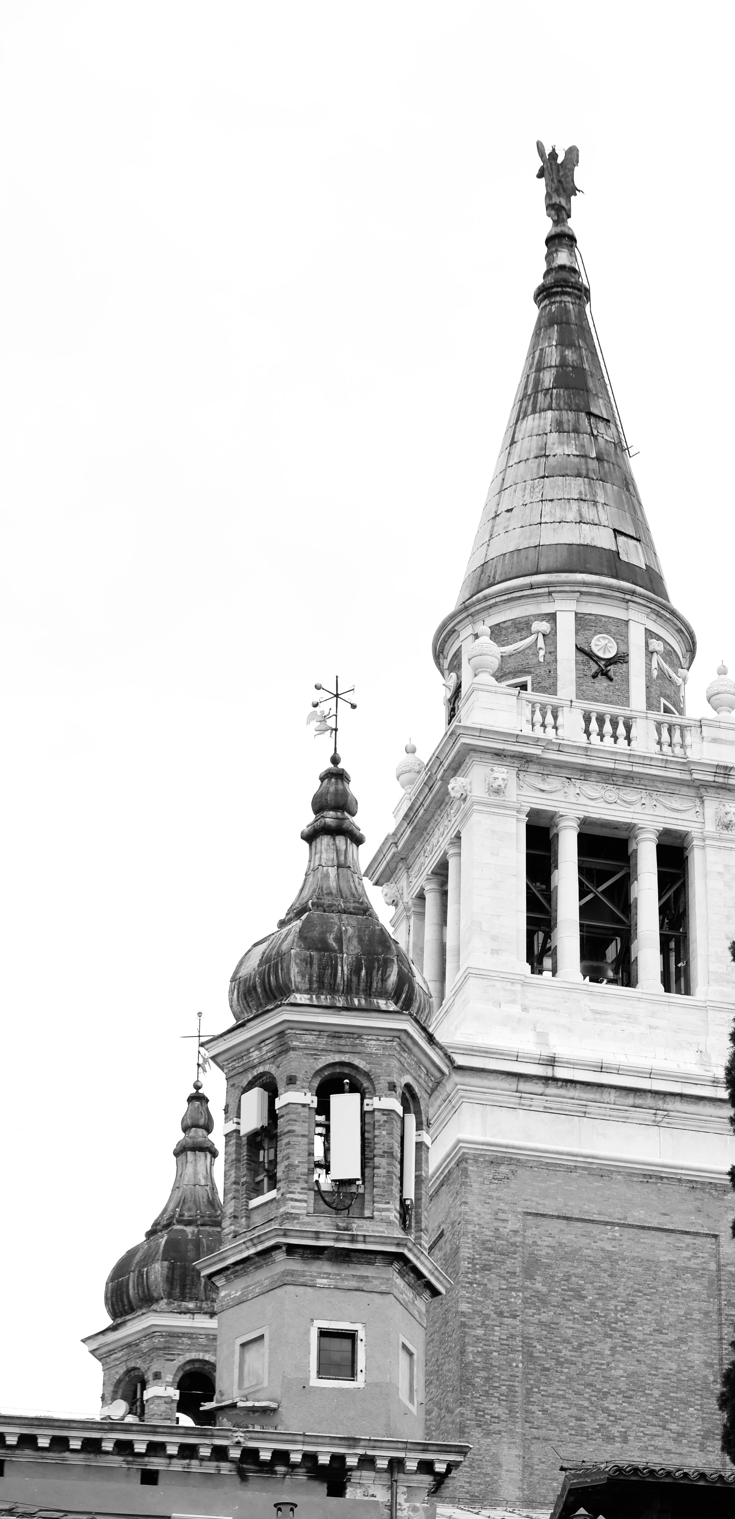 Black and white photo of a tall, ornate church steeple with clock, decorative elements, and multiple smaller domed towers.