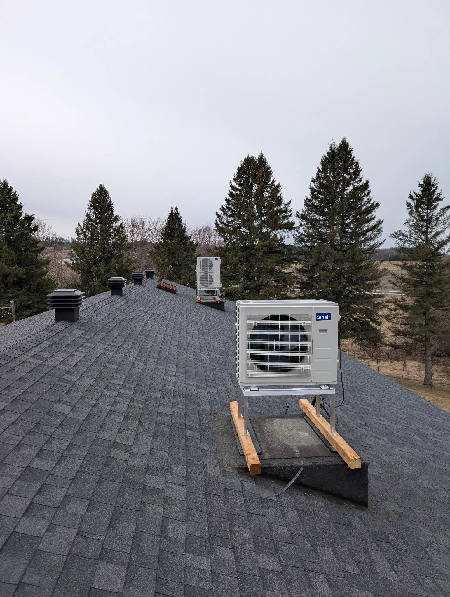 Un toit en bardeaux noirs avec deux unités extérieures de climatisation et plusieurs évents.