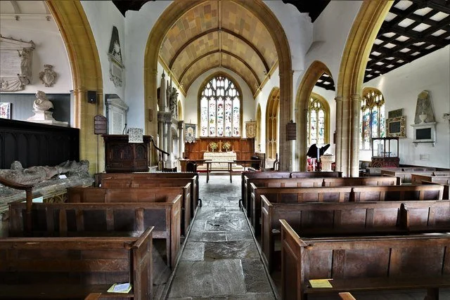 Interior of a HintonSt George church with wooden pews, stained glass windows, stone walls, and religious sculptures.