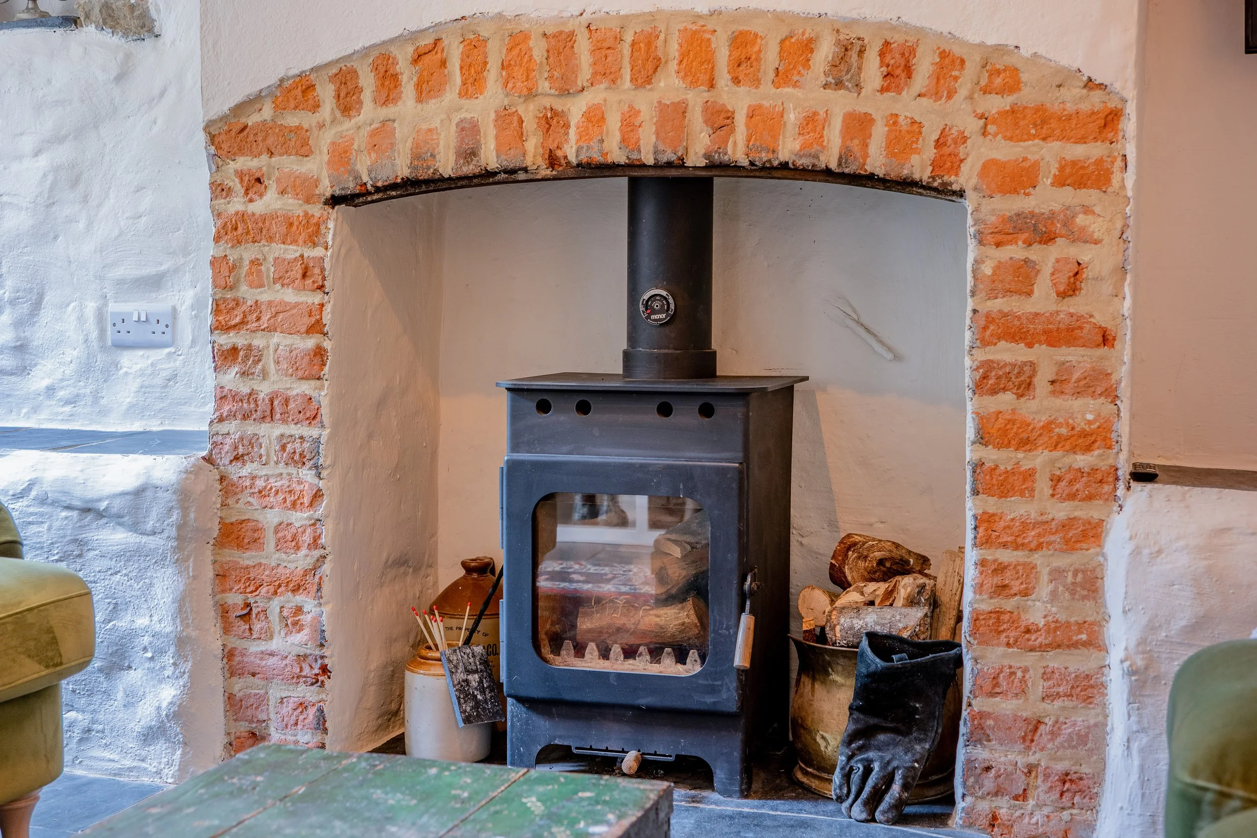 Wood stove inside a brick and plaster fireplace with logs and fire tools nearby