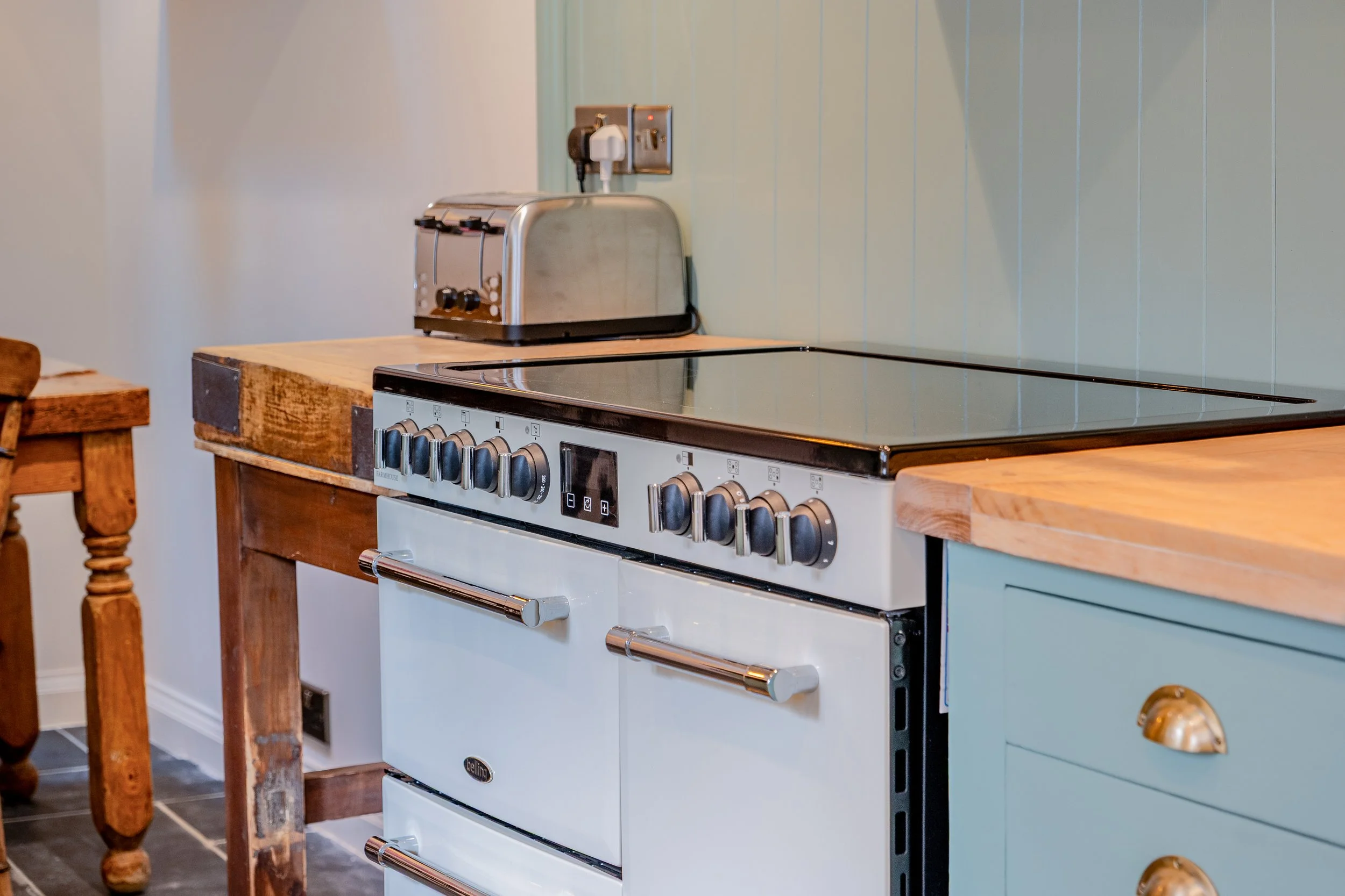 A kitchen with a white stove, a wooden countertop, and a toaster on the countertop near the wall with green paneling.
