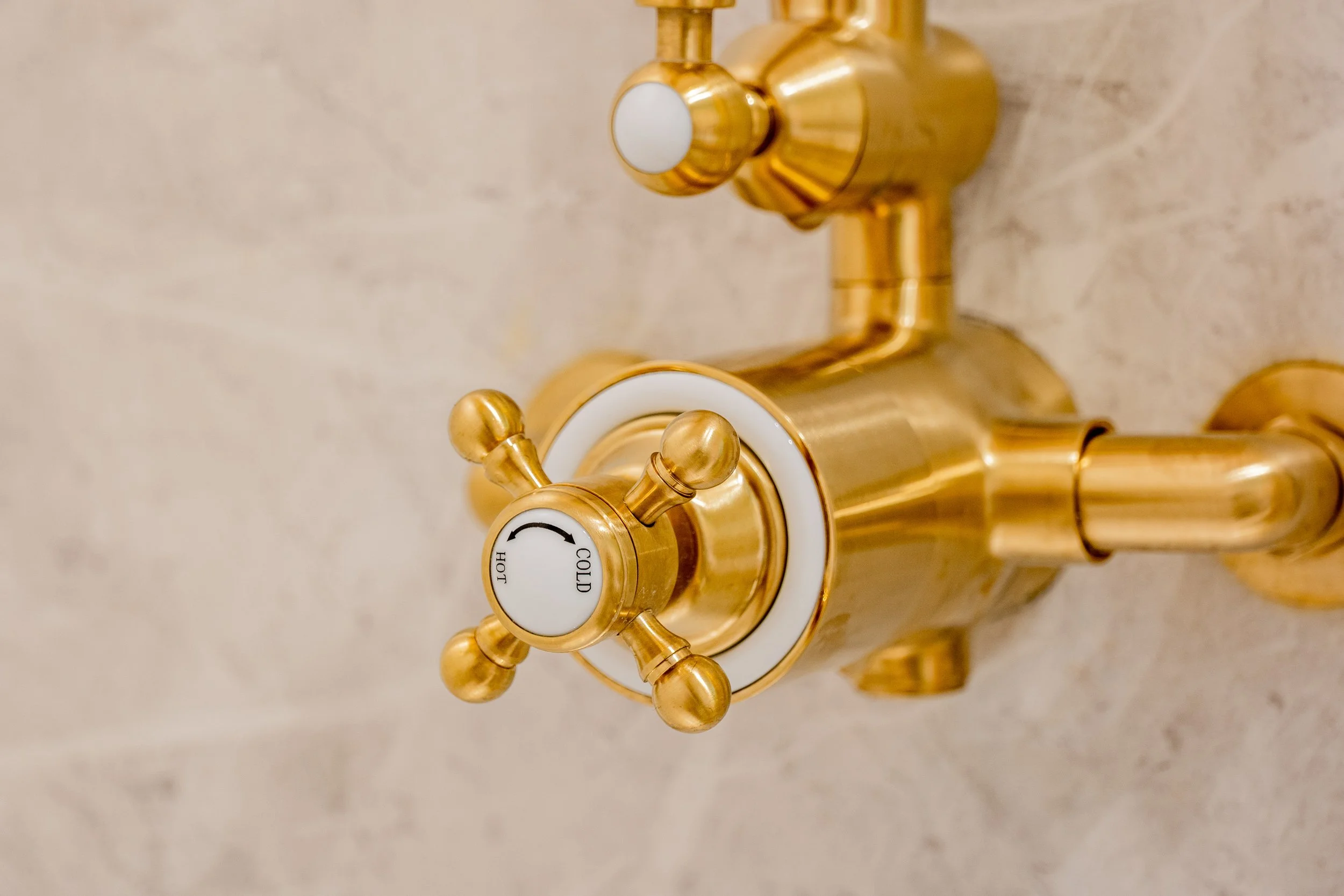 Close-up of a gold-colored faucet handle with a white circular center labeled 'HOT' and 'COLD', mounted on a beige textured countertop.