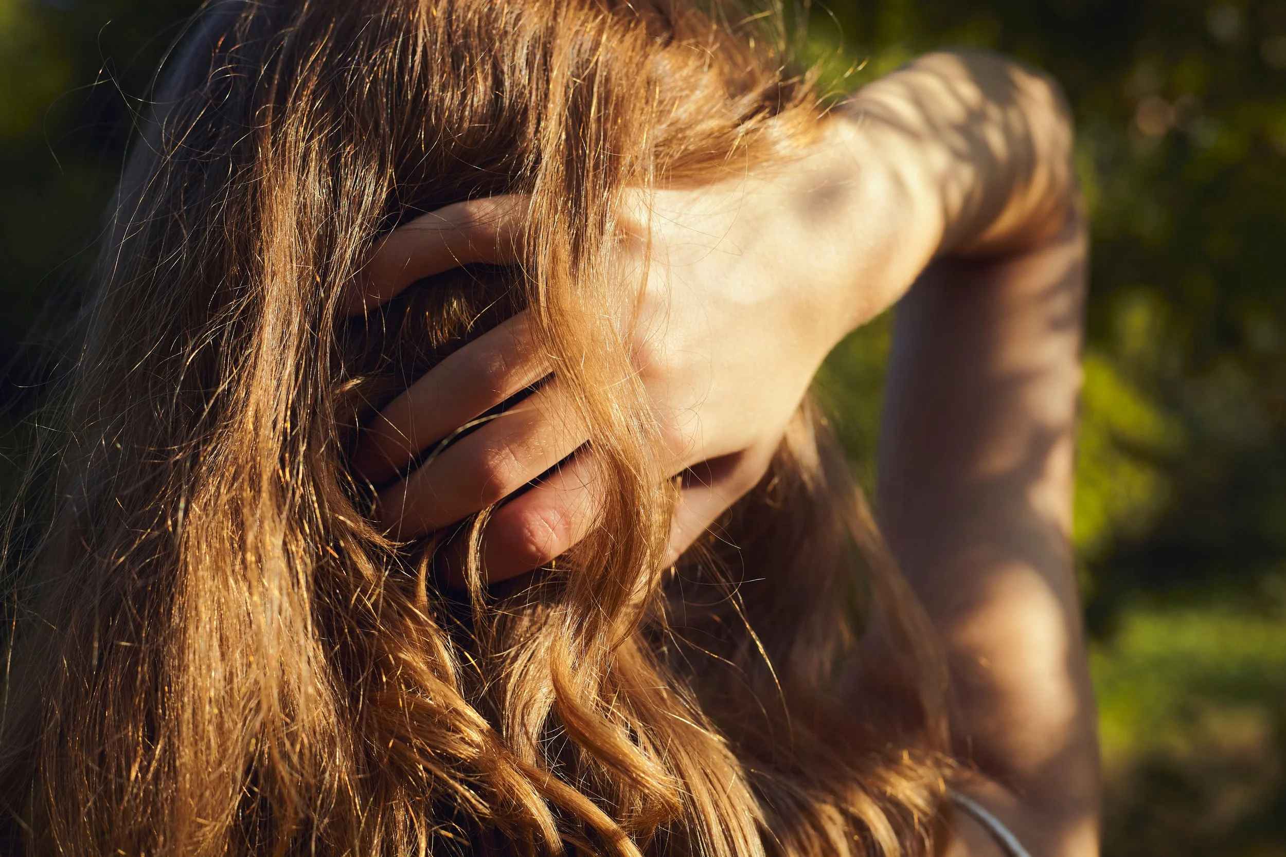 Una donna con capelli ricci rossi si copre il volto con la mano, visibile una foresta sullo sfondo