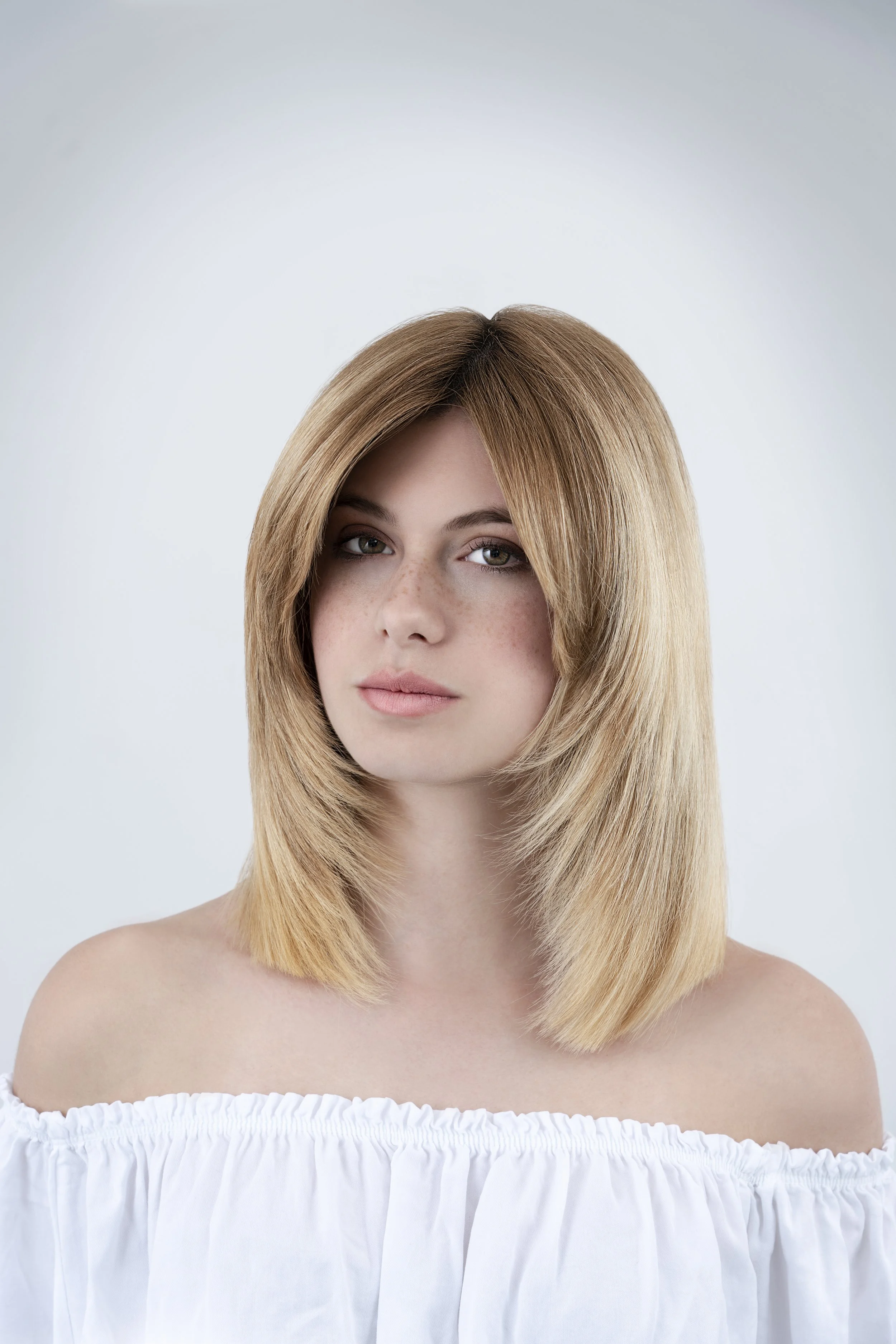 Ragazza con capelli castani a forcina, pelle chiara con lentiggini, abbigliamento bianco bianco a spalle scoperte.