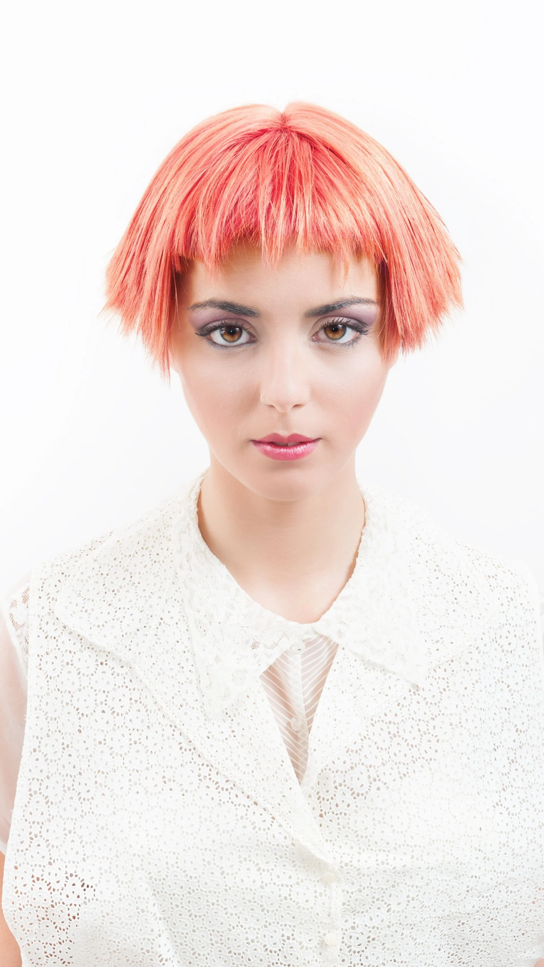 Ragazza con capelli corti e rosa, abbigliamento bianco con motivo traforato, sfondo bianco.