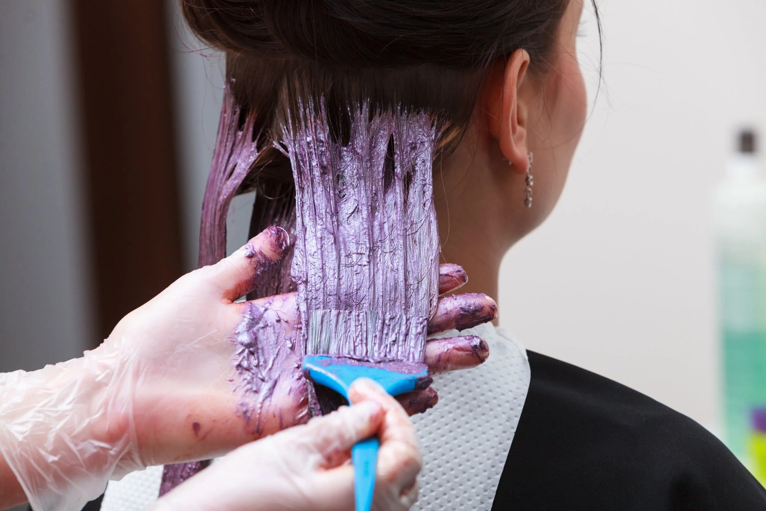 Una persona sta ricevendo un trattamento di colore dei capelli, applicando tinta viola sulla nuca e sui capelli.