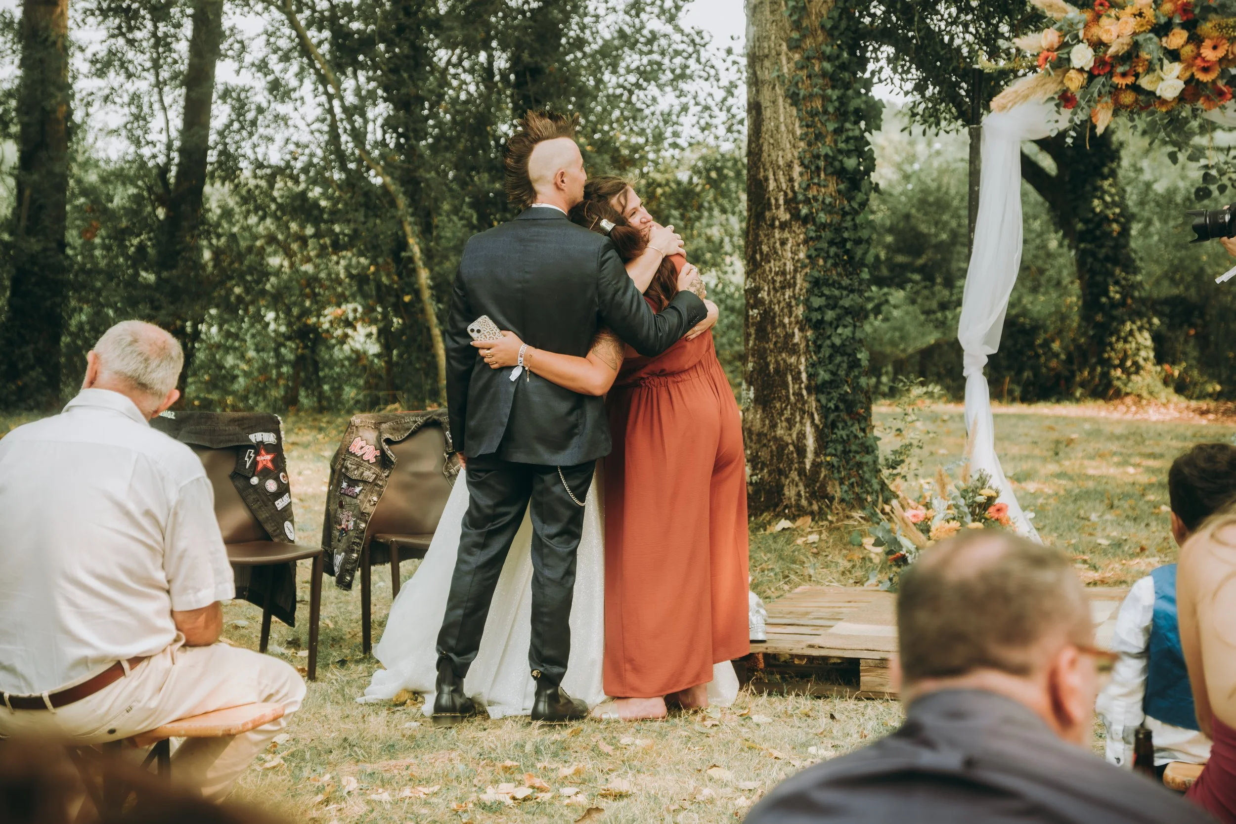 Deux personnes en vêtements de mariage se serrent dans une étreinte lors d'une cérémonie extérieure en forêt.