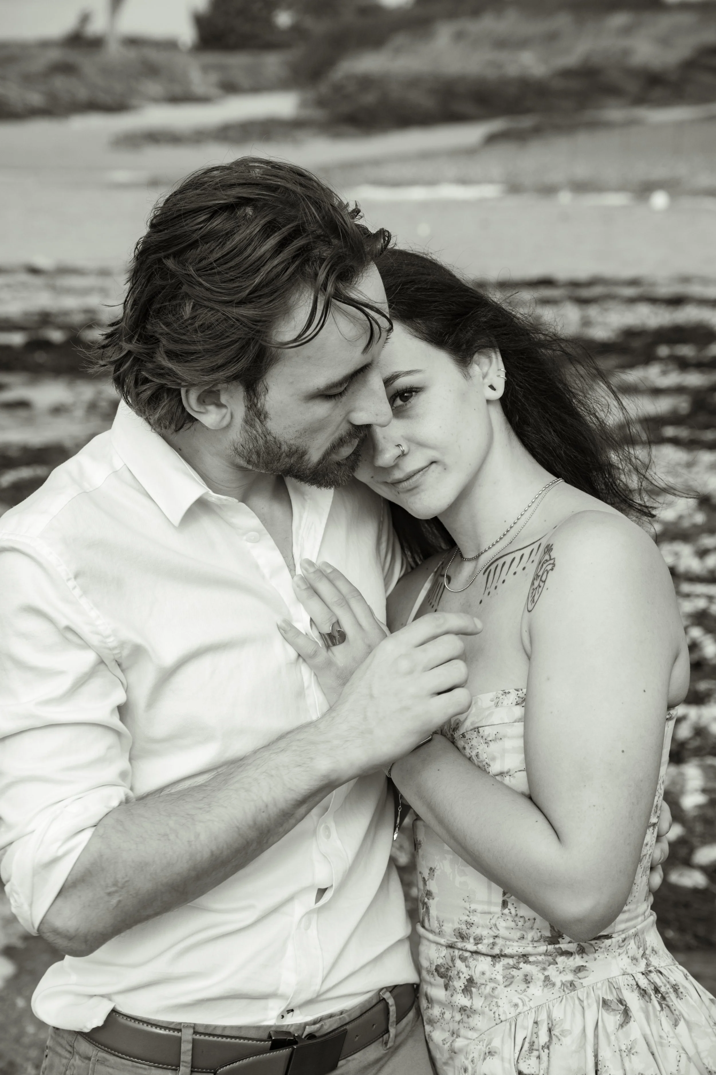 Un couple enembrassé sur la plage en noir et blanc, avec des vagues en arrière-plan.