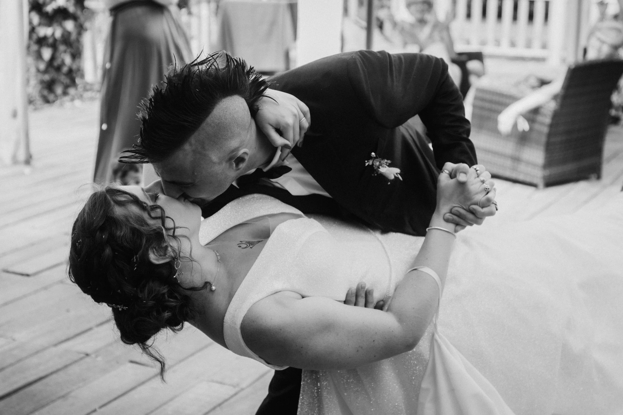 Un couple danse lors d'un mariage, l'homme porte un costume noir et la femme une robe blanche, en noir et blanc.