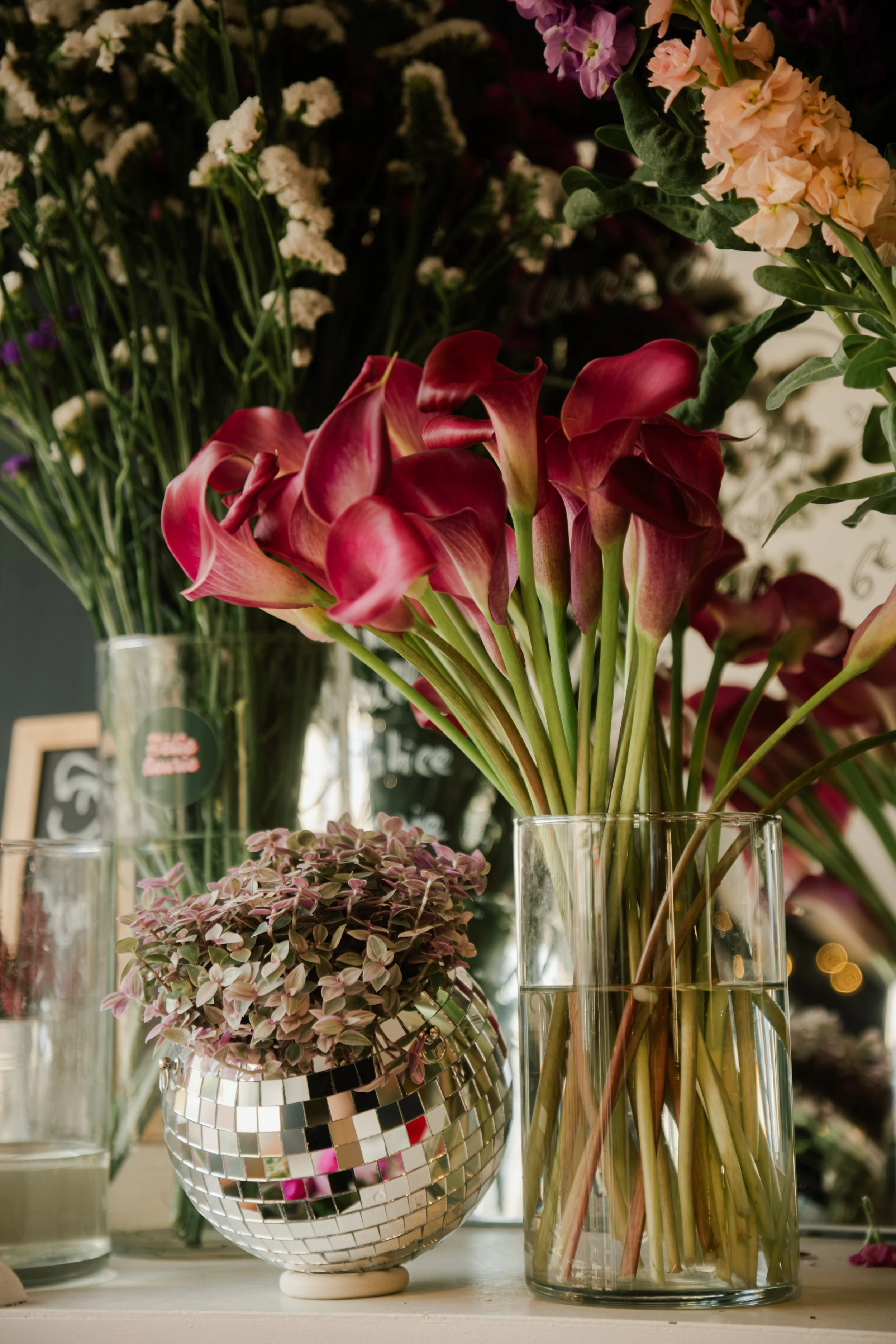 Vases contenant des fleurs roses et blanches, avec d'autres fleurs en arrière-plan, dans un décor intérieur.