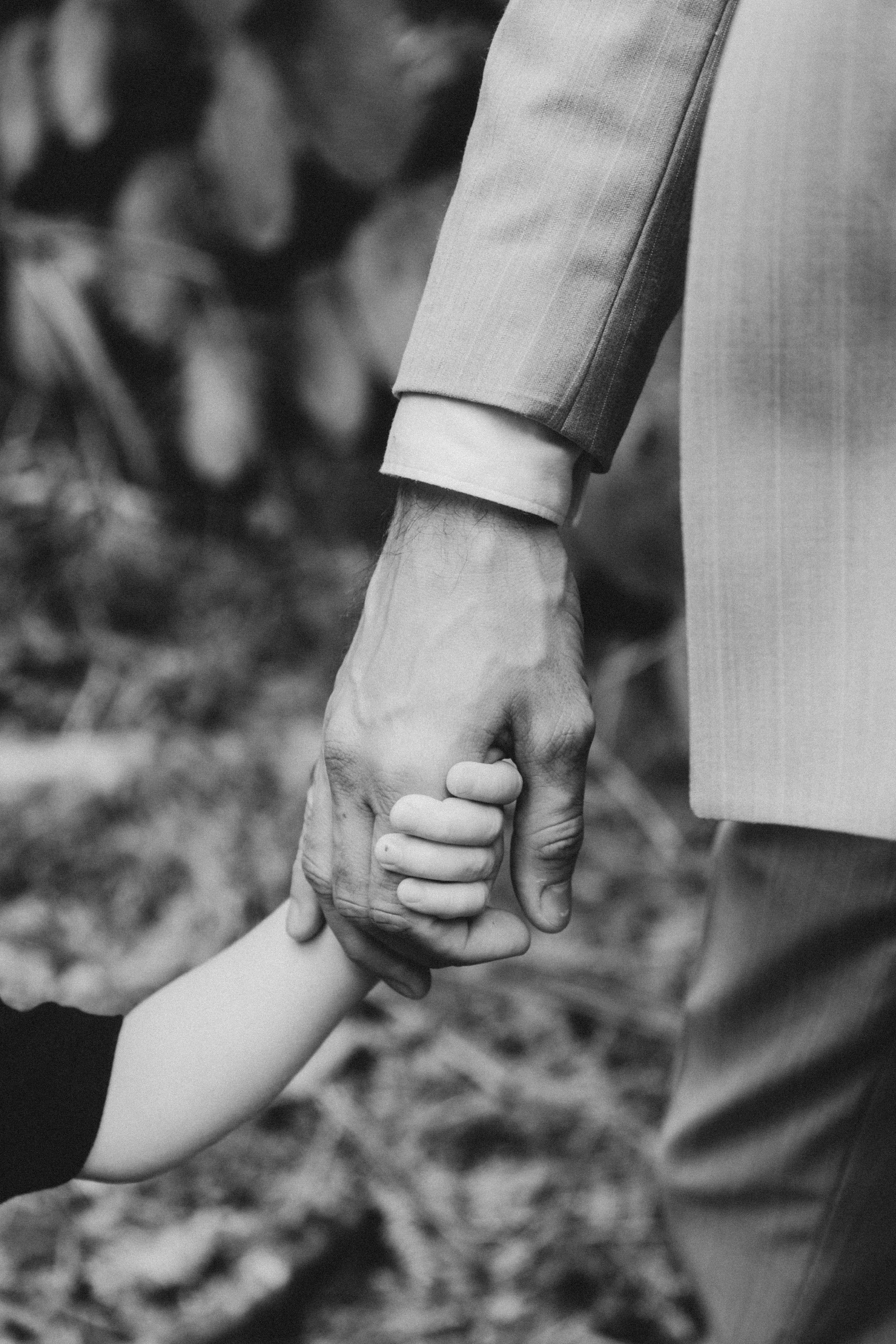 Une main d'adulte tenant la main d'un enfant, en noir et blanc.