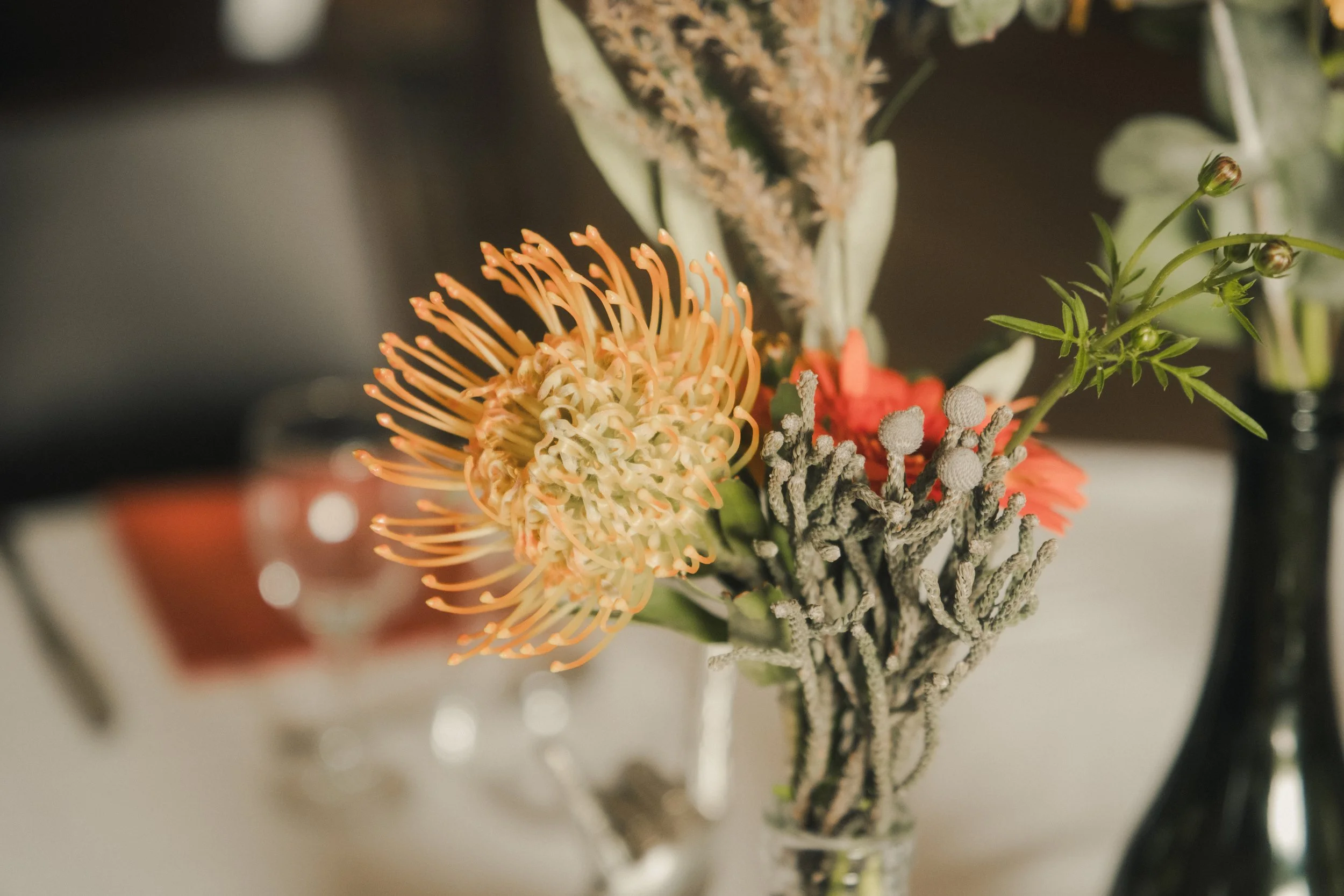 Bouquet de fleurs avec une fleur orange à longues étamines, accompagnée d'autres fleurs et feuillages dans un vase en verre.