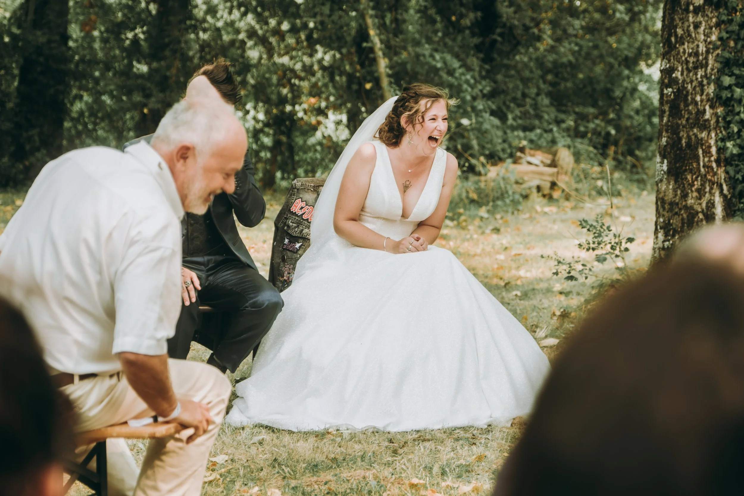 Une mariée rit en plein air, entourée de plusieurs personnes, dans un environnement forestier